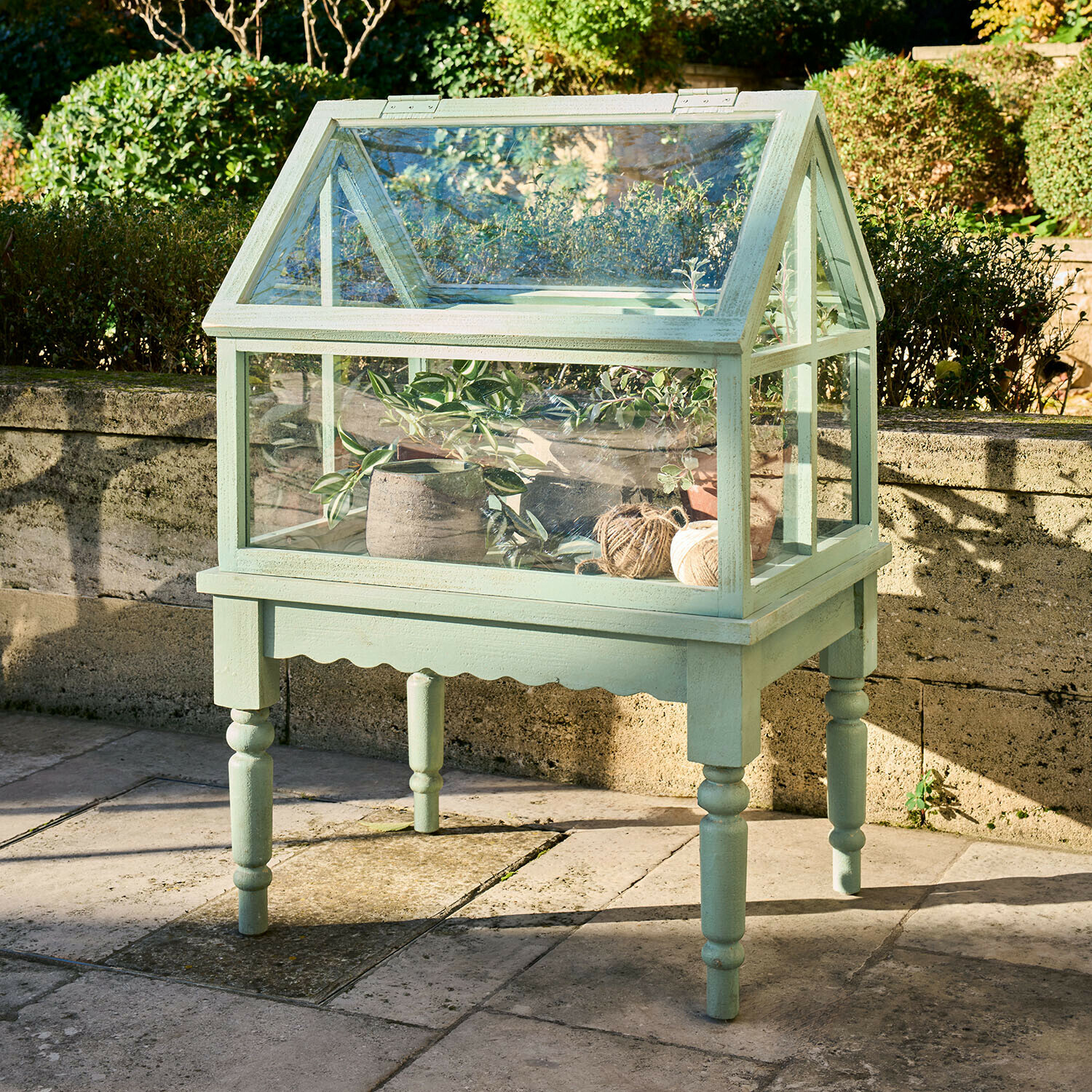 Kleine groene houten kas op poten met planten en garenrollen voor de tuin