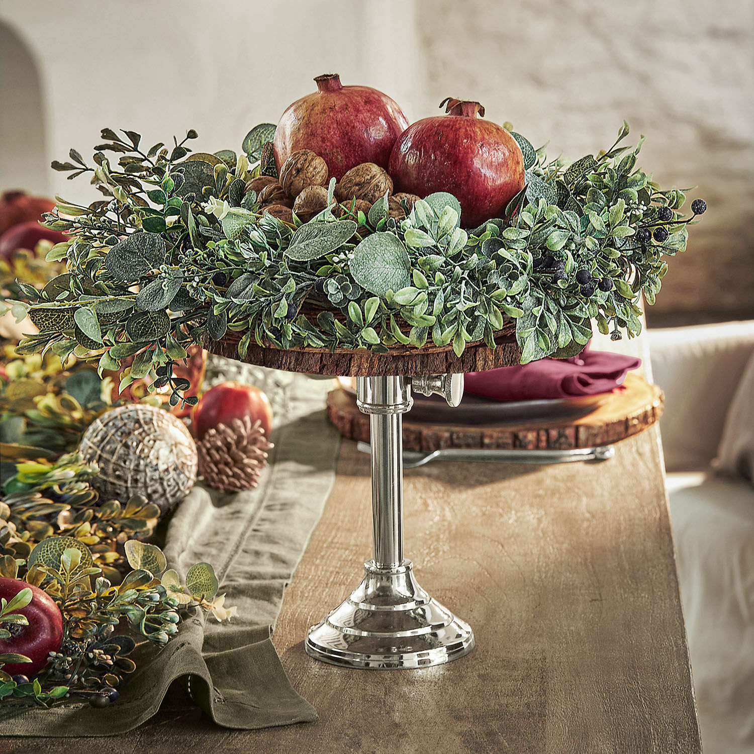 Etagère Danice II Decoratieve houten en metalen schaal met granaatappels, walnoten en groen blad op houten tafel