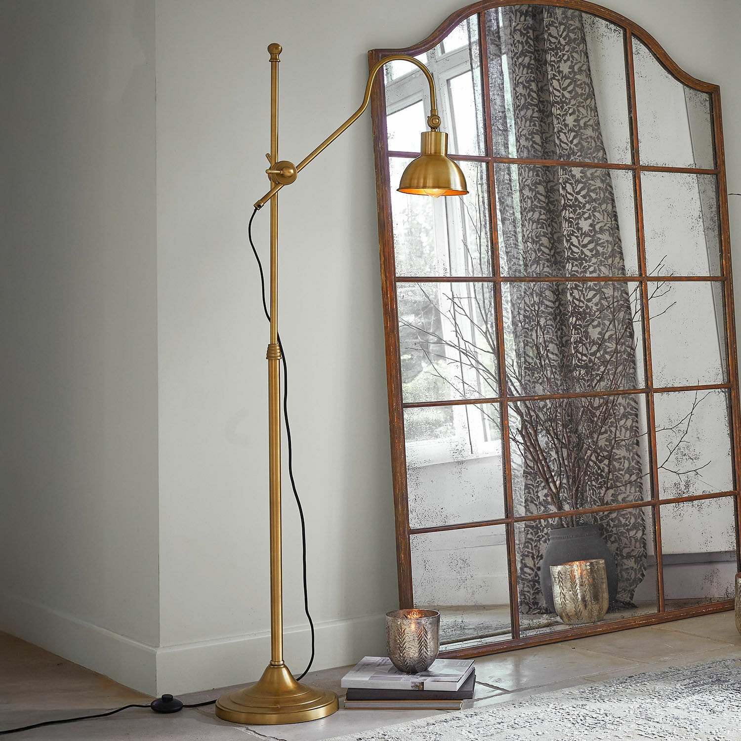 Gouden metalen vloerlamp met verstelbare arm naast een grote vintage spiegel