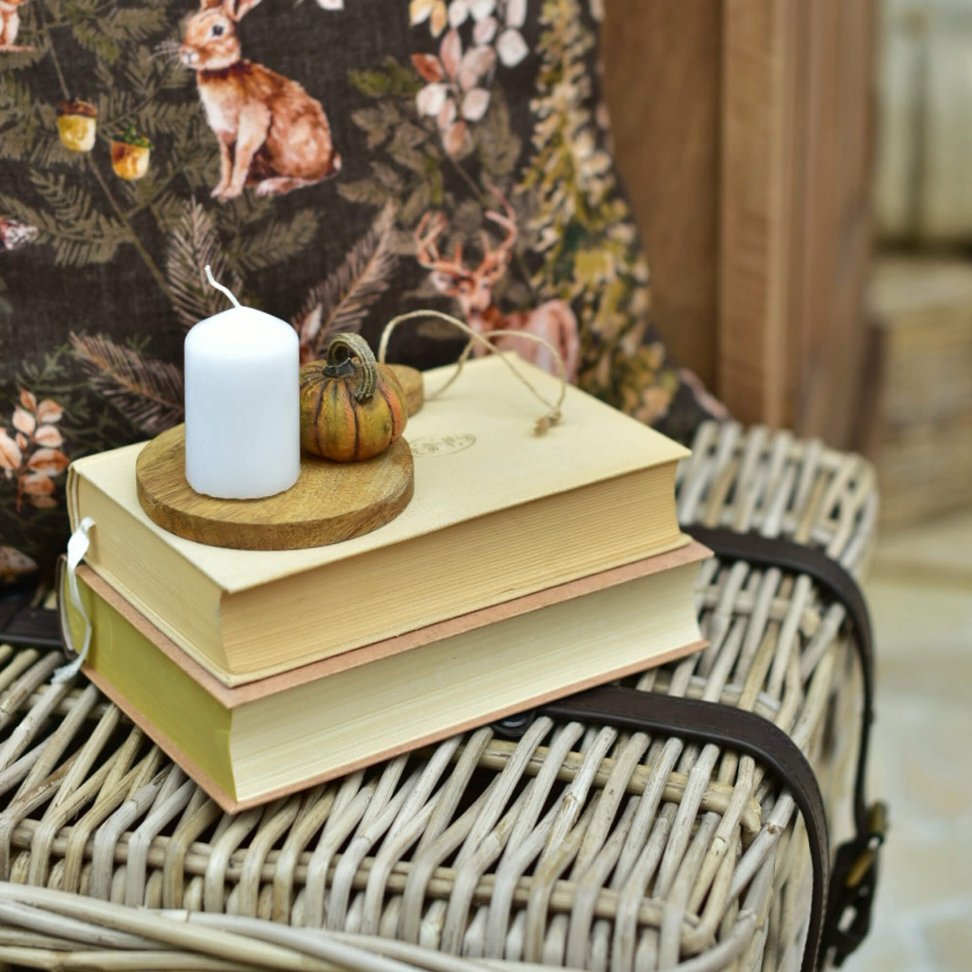Witte kaars en kleine decoratieve pompoen op houten plank op stapel boeken op een rieten koffer