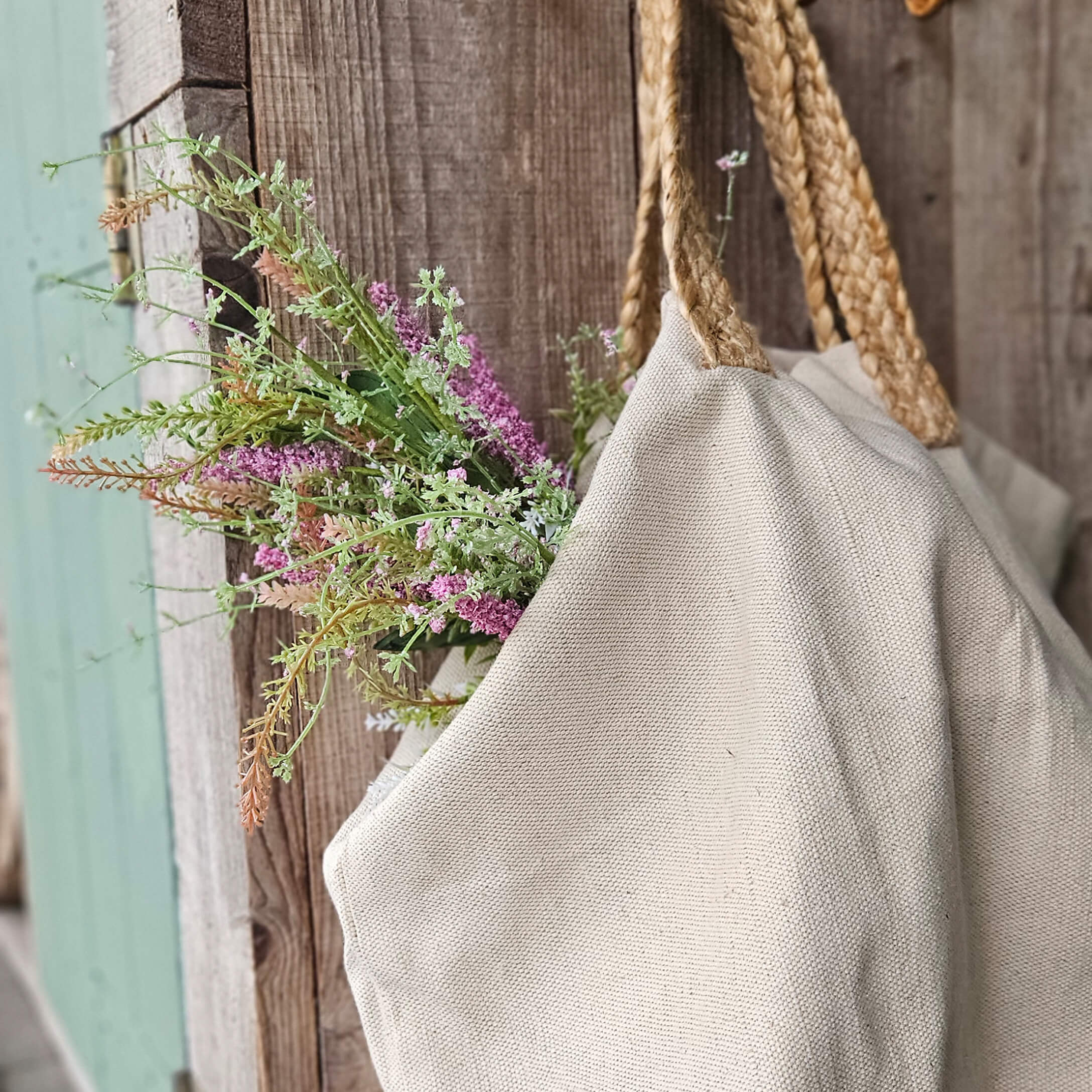 Beige tas van natuurlijk materiaal met gevlochten handvatten en bloemen tegen rustiek hout