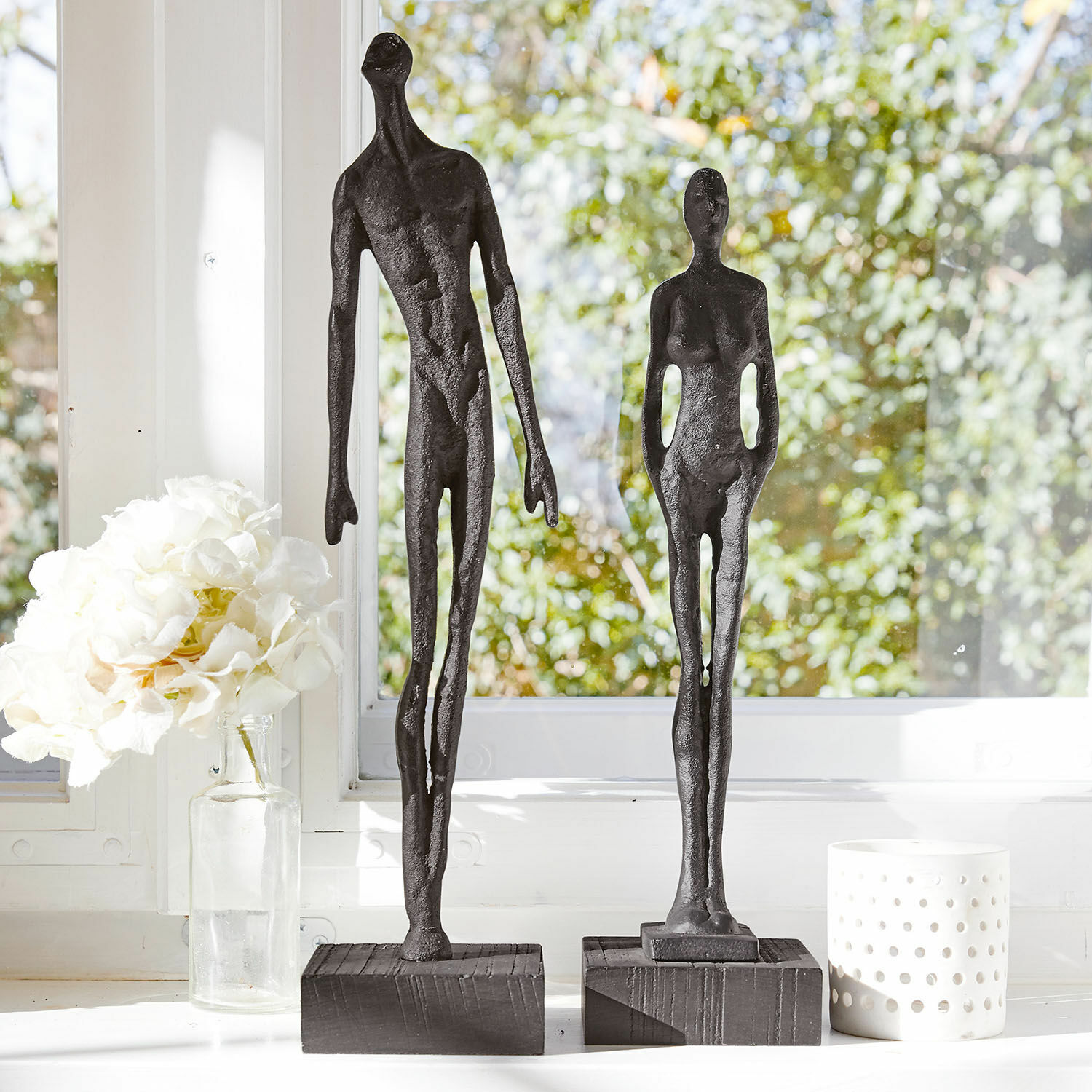 Beeldje set van 2 Perce Twee zwarte metalen beeldjes van menselijke figuren op houten sokkels bij een raam met witte decoraties