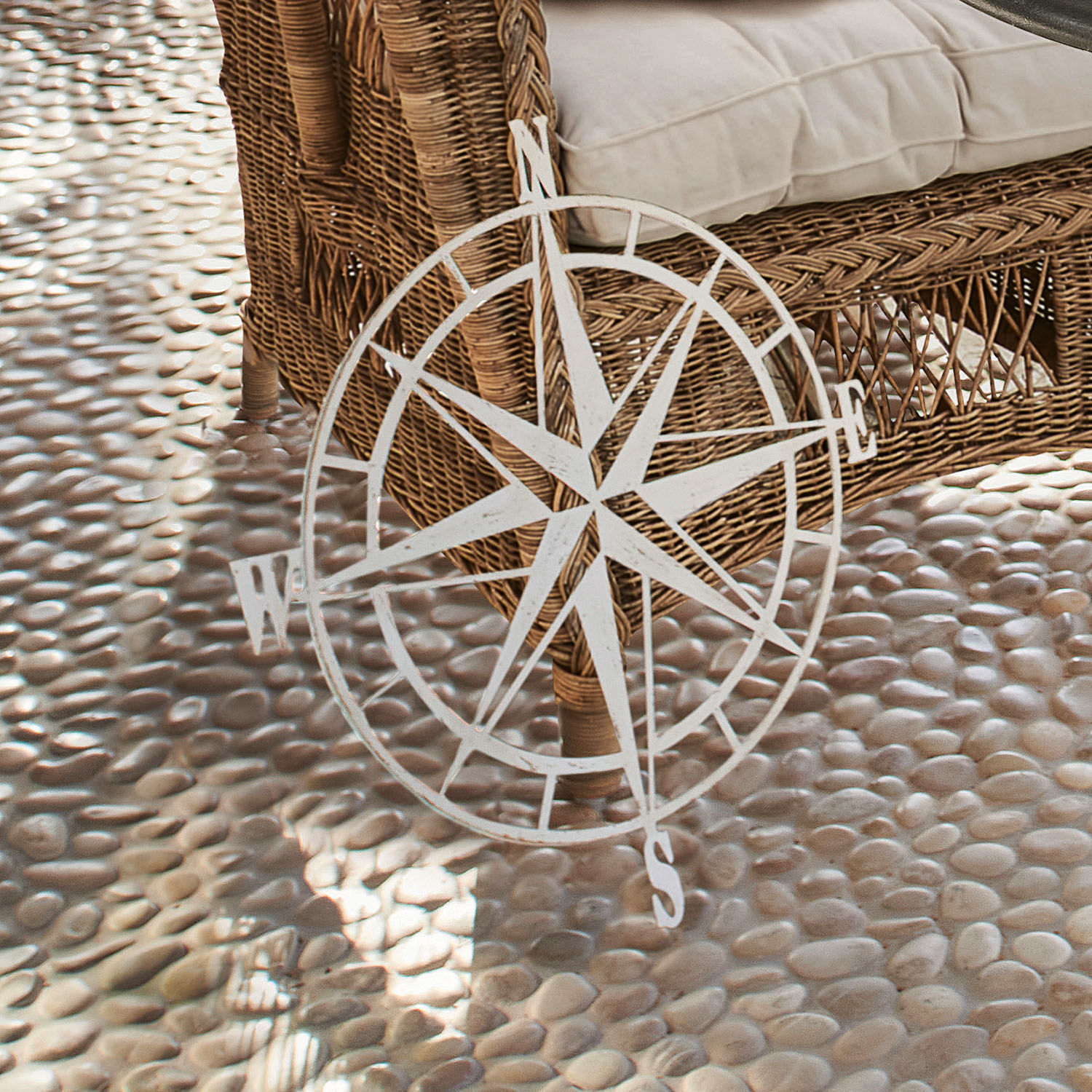Decoratieve witte metalen windroos voor een rotan stoel op een kiezelstenen vloer