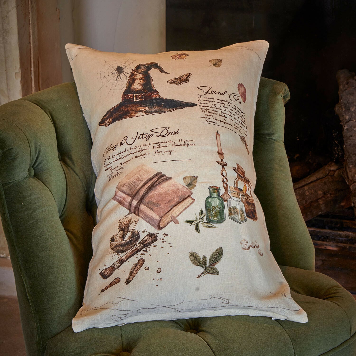 Kussenhoes Maerlinna Beige linnen kussen met print van zwarte hoed, boek en kruiden op groene stoel