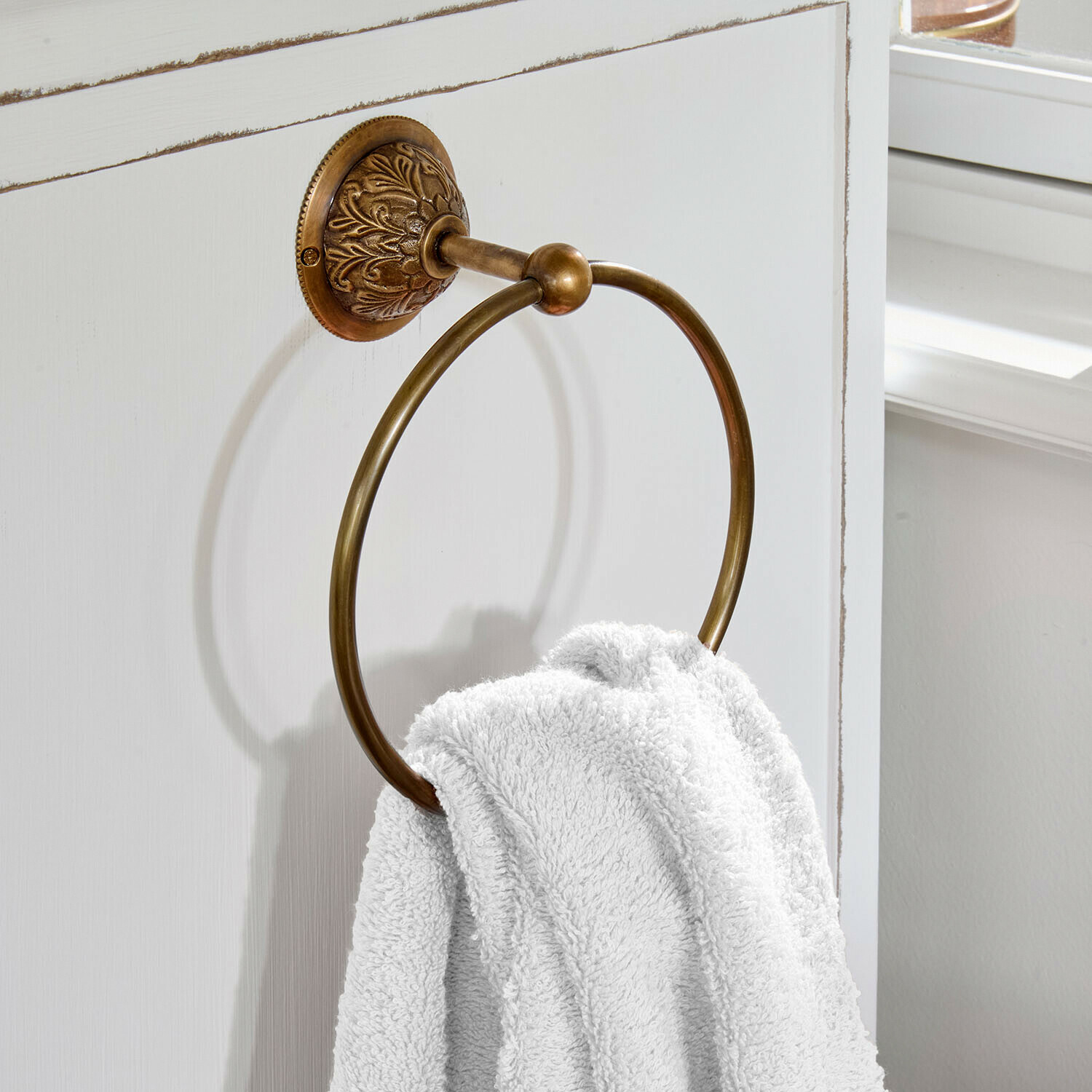 Ronde handdoekring van messing met decoratieve bevestiging aan witte badkamerdeur