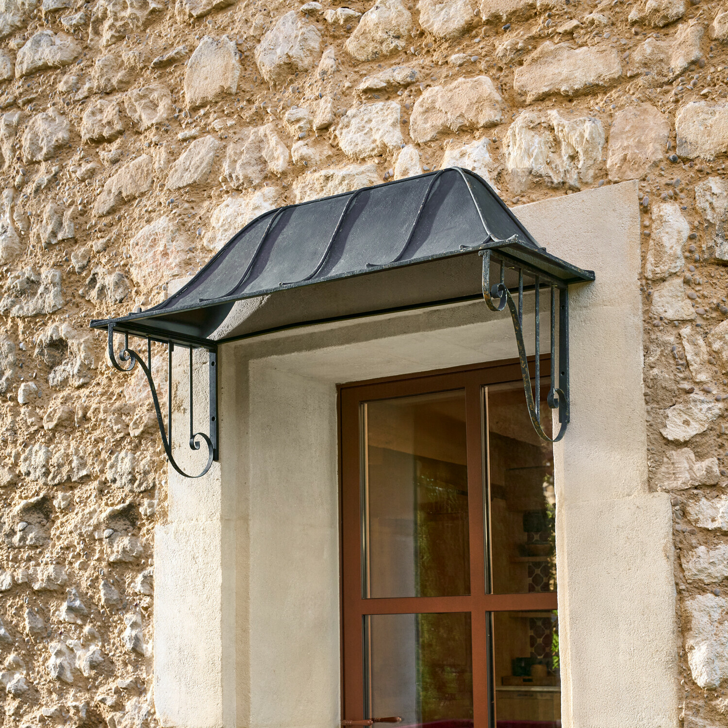 Zwart metalen luifel boven raam op stenen muur, bescherming tegen regen en weersinvloeden