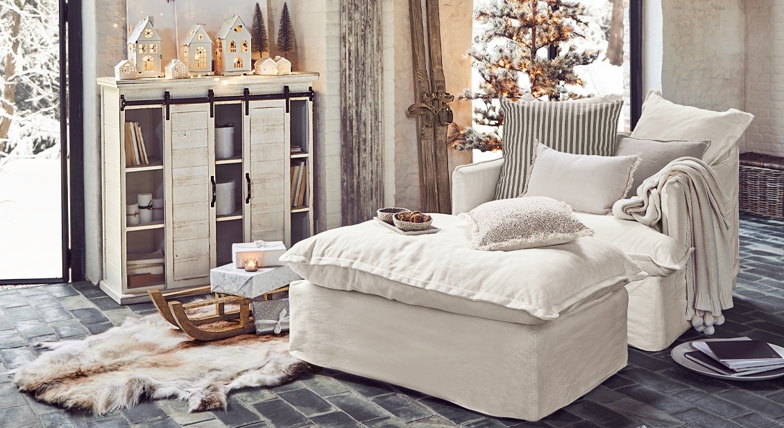 Gezellige witte fauteuil met voetenbank en decoratieve kussens in winterse kamer met houten kast