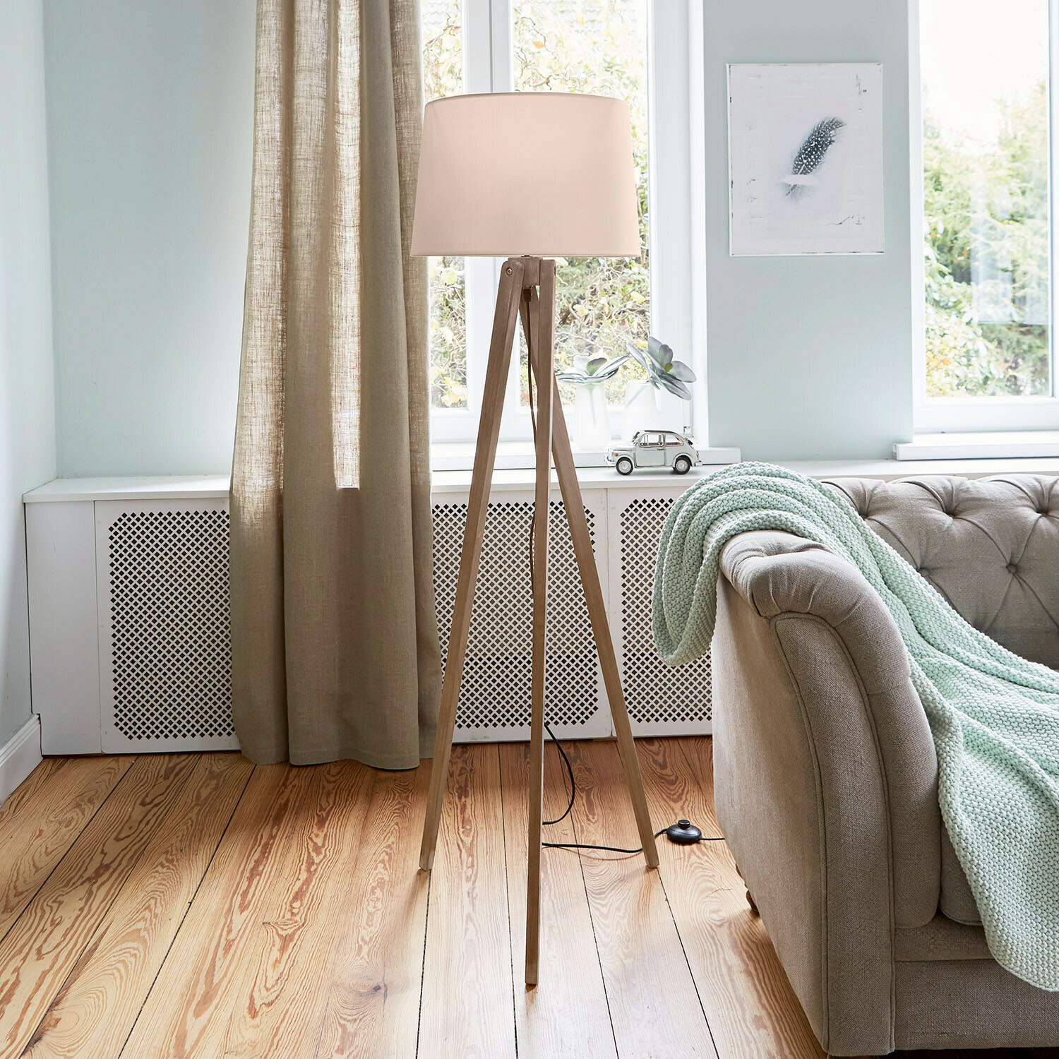Staande lamp met houten voet en crèmekleurige kap in lichte woonkamer met bank en gebreide deken