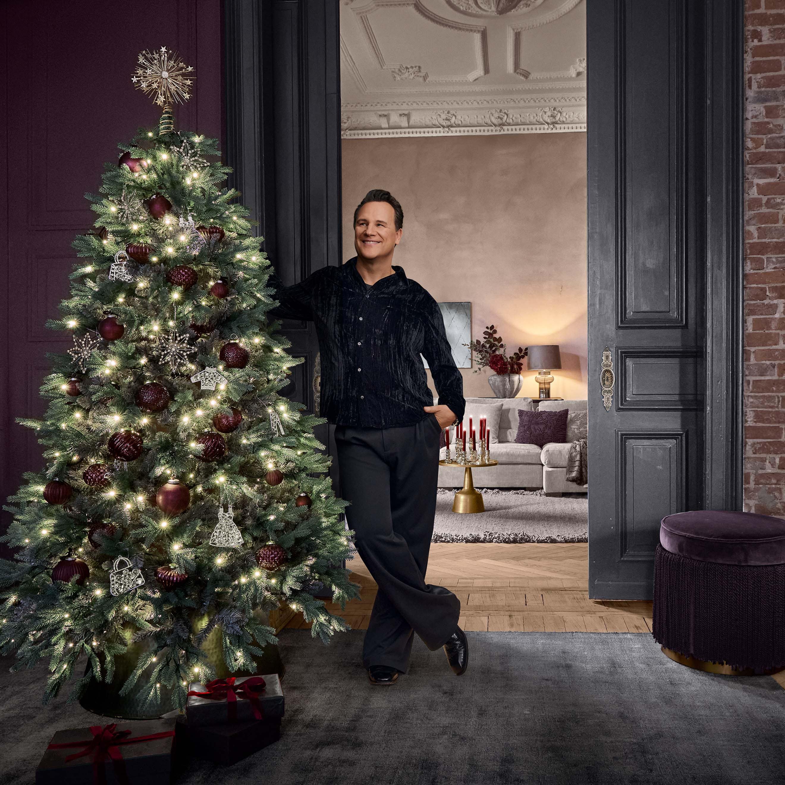 Kerstboom met rode en zilveren versieringen en lichtjes in een stijlvolle kamer met man.