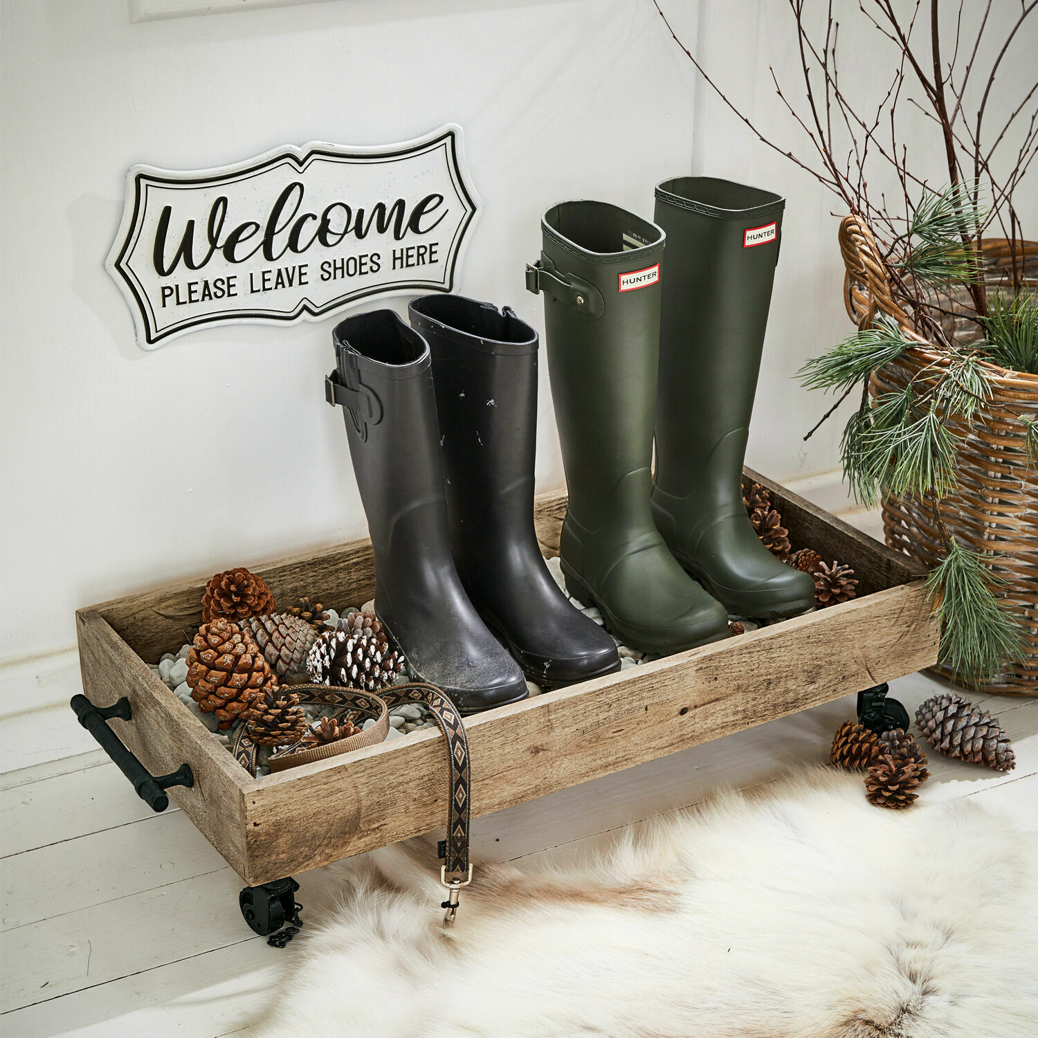 Houten dienblad op wieltjes met stenen en dennenappels, zwarte en groene rubberlaarzen in de hal
