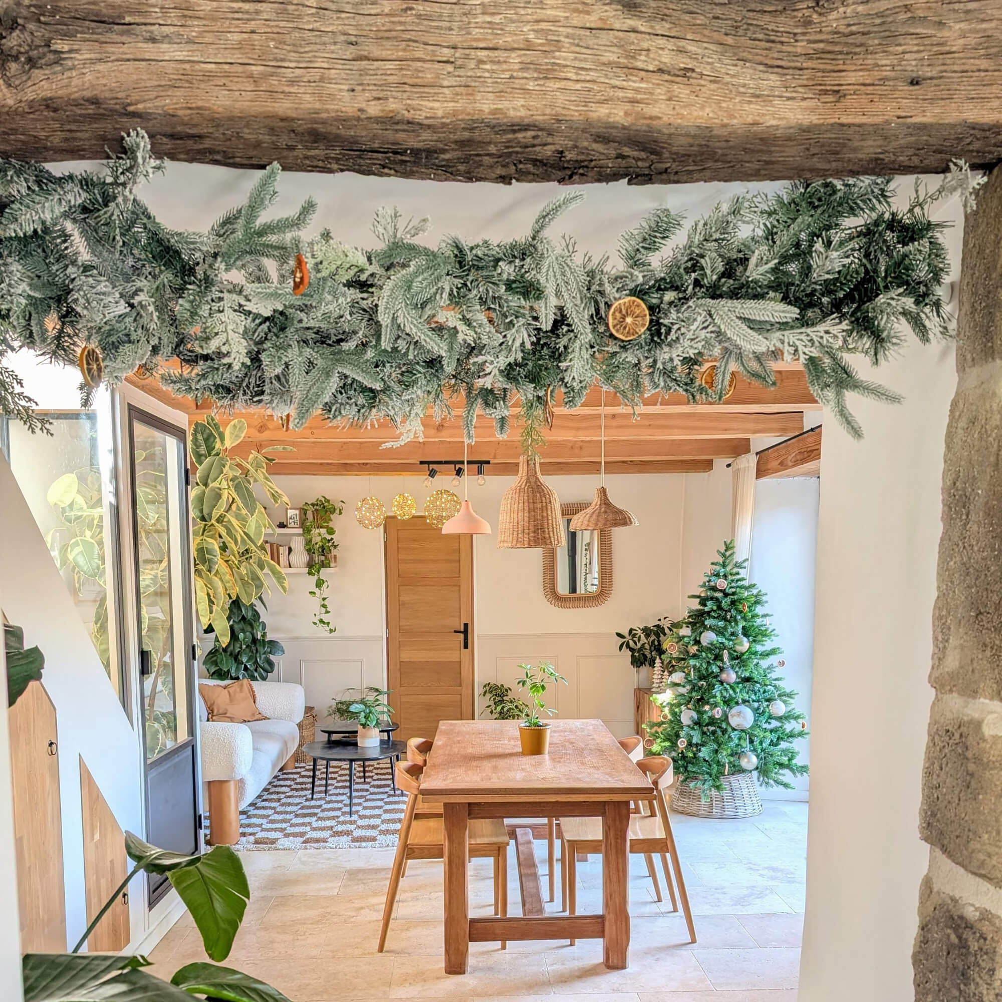 Gezellige ruimte met houten tafel, kerstboom en groene slinger met gedroogde sinaasappelschijfjes