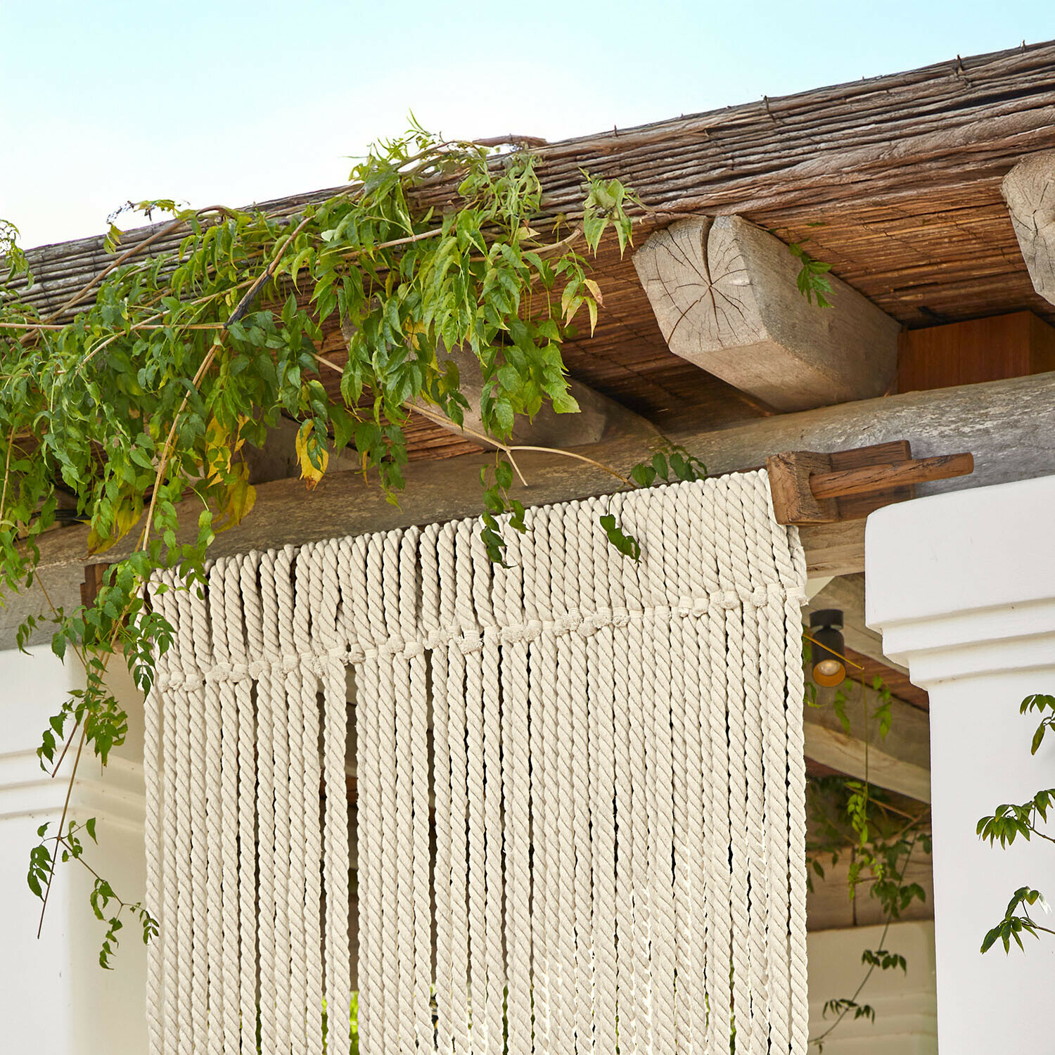 Decoratief gordijn van wit katoenen touw aan houten constructie met groene bladeren