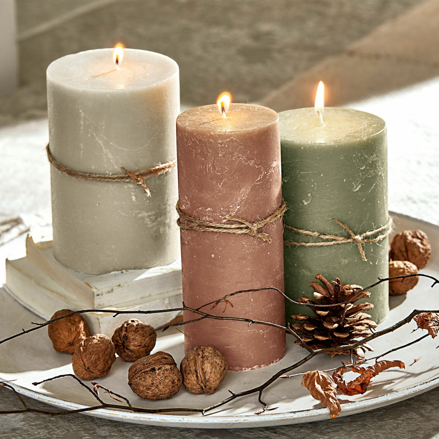 Drie brandende kaarsen van was in beige, roze en groen op een decoratief dienblad met noten en takken