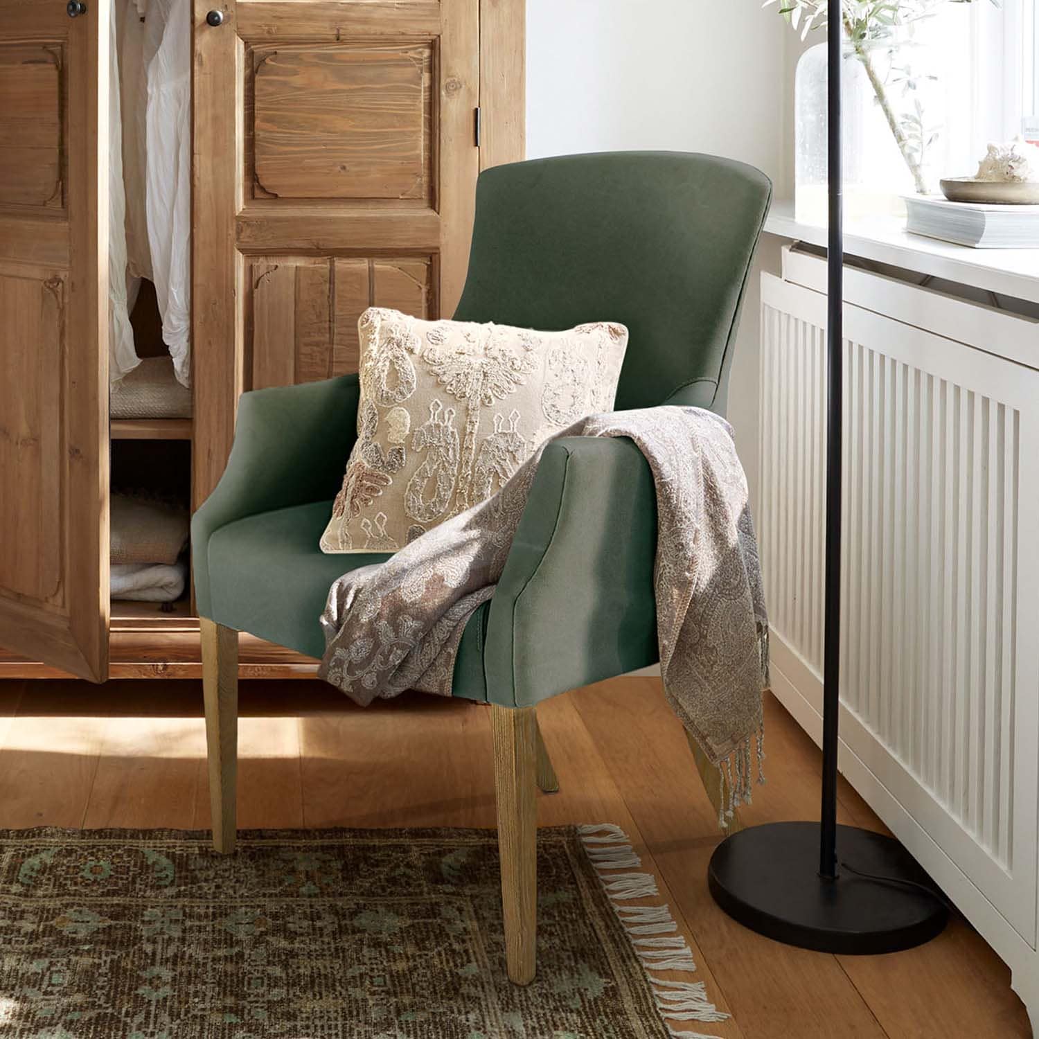 Groene gestoffeerde stoel met houten poten, decoratief kussen en grijze plaid in gezellige ruimte