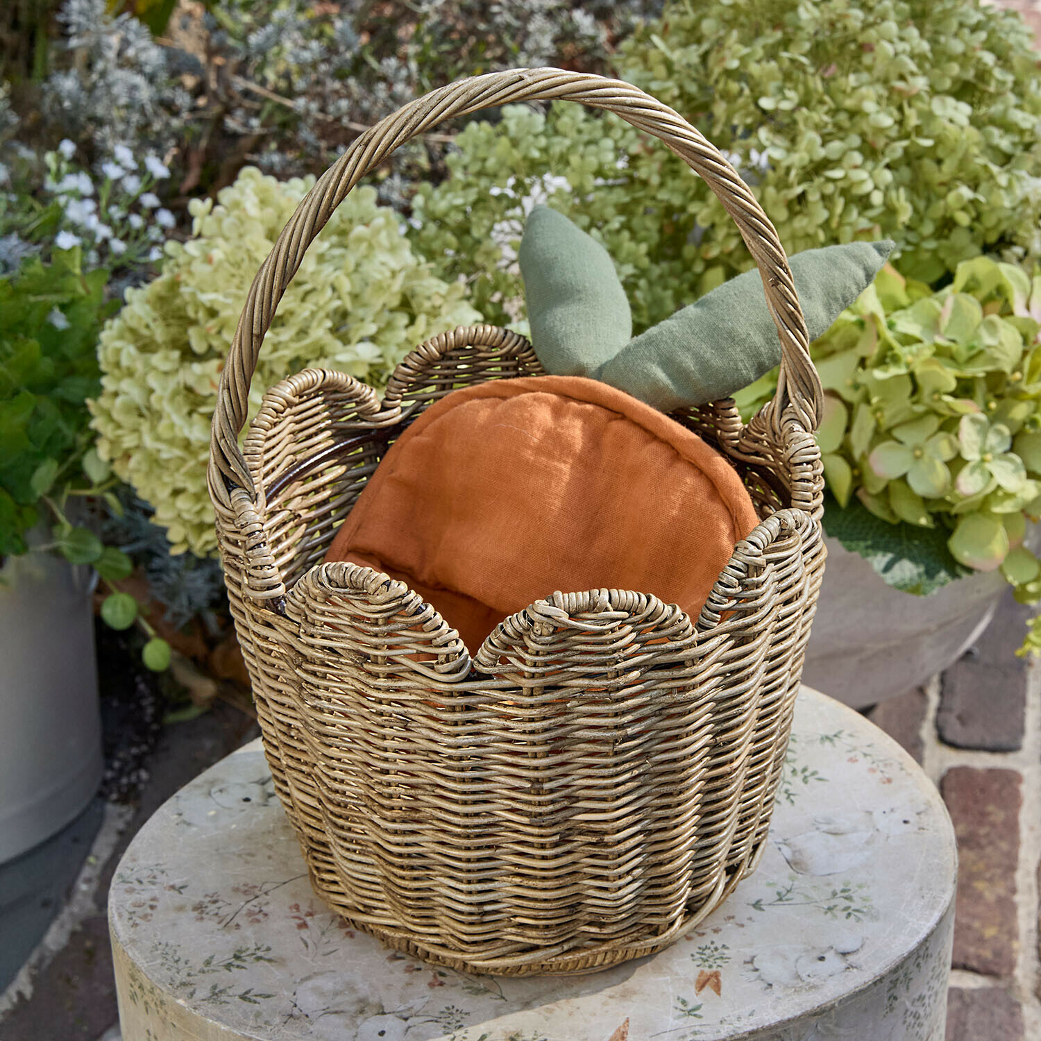 Rieten mand met oranje kussen en groene bladeren, tuindecoratie op ronde tafel