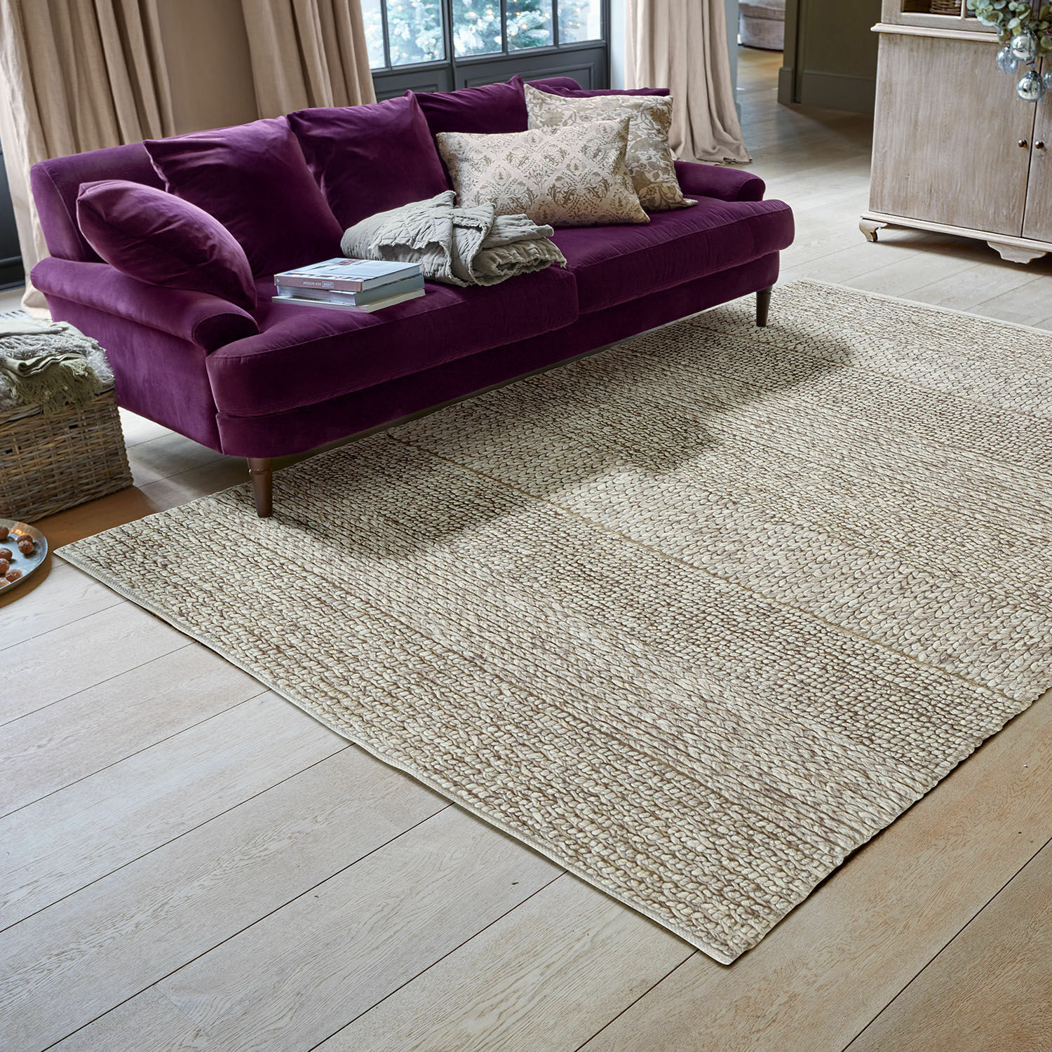 Vloerkleed Welezas Lichtbeige vloerkleed van natuurlijk materiaal op houten vloer onder paarse fluwelen bank