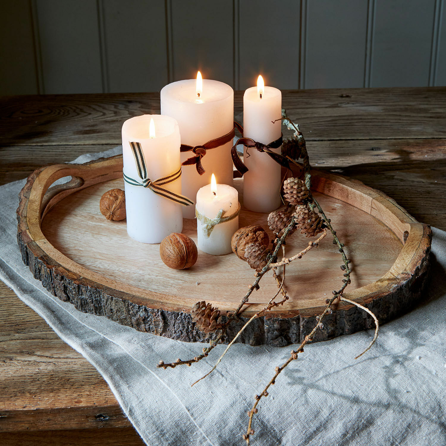 Houten dienblad met natuurlijke schors, vier brandende witte kaarsen en decoratie van noten en dennenappels