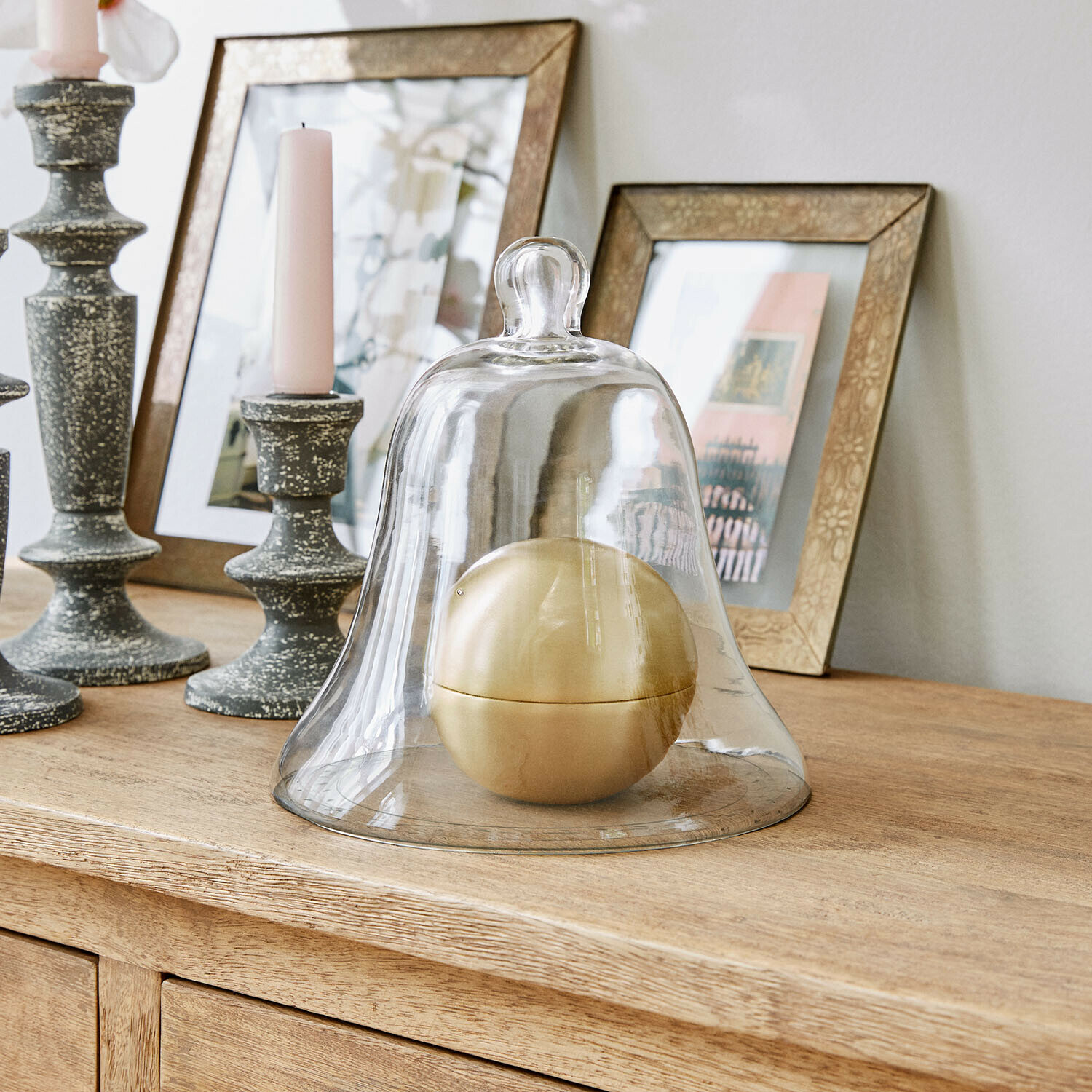 Glazen stolp van helder glas met gouden bol als decoratie op een licht houten meubel