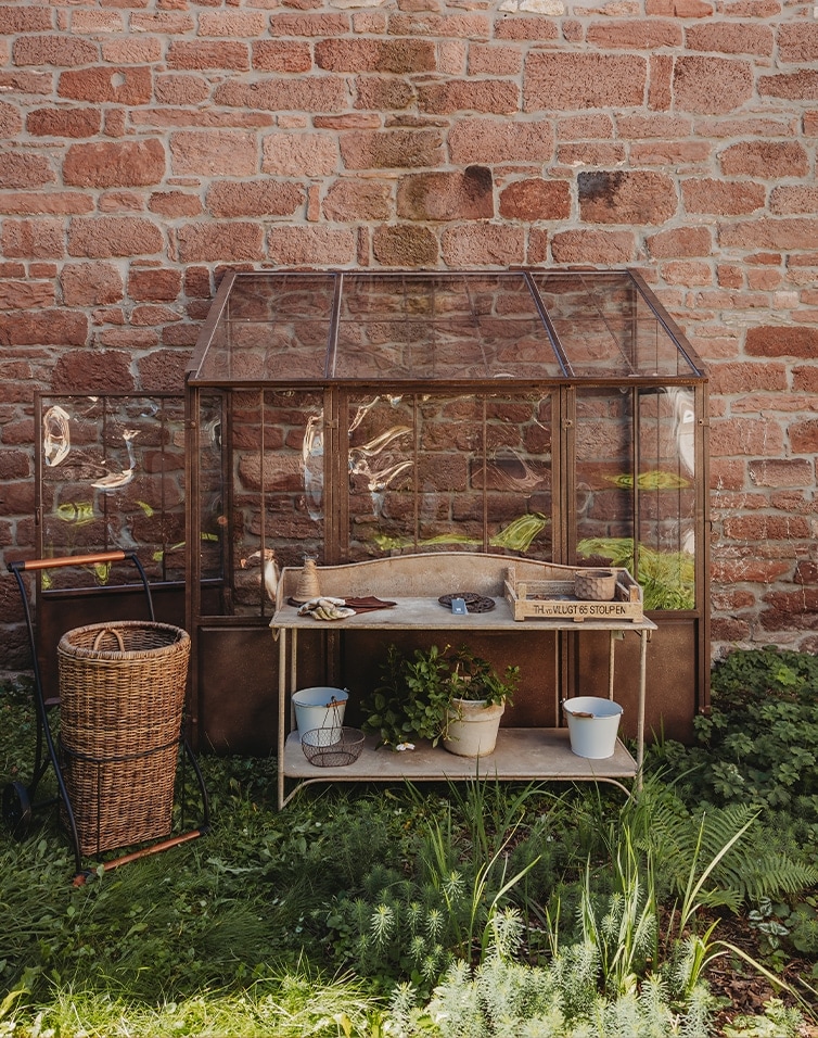 Tuinserre met metalen frame en houten werktafel voor een bakstenen muur