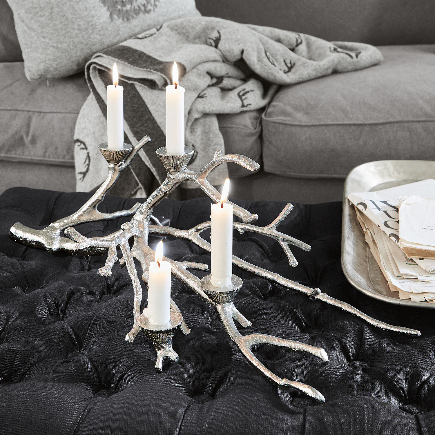 Zilverkleurige metalen kandelaar in takvorm op zwarte bekleding in woonkamer