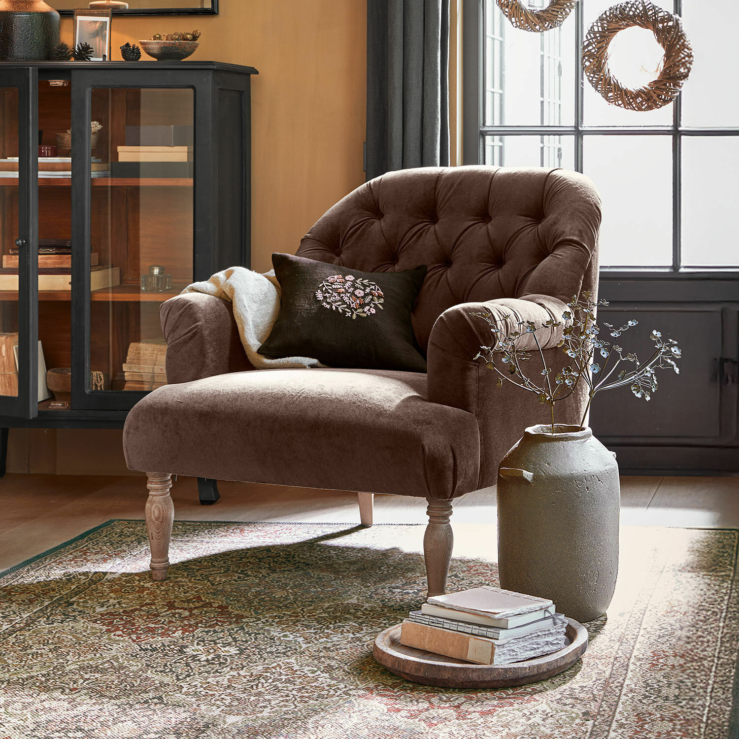 Bruine fluwelen fauteuil met gestikte rugleuning en houten poten in gezellige woonkamer met tapijt