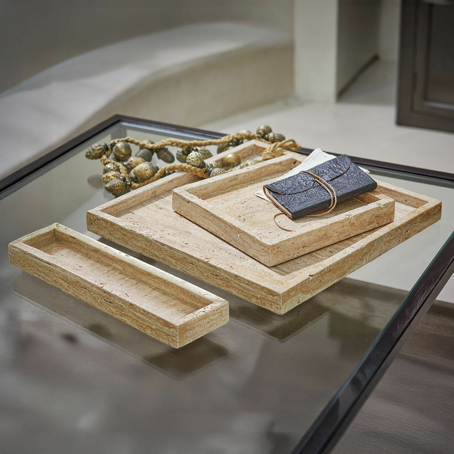 Set van drie rechthoekige beige stenen trays op een glazen tafel met zwarte rand
