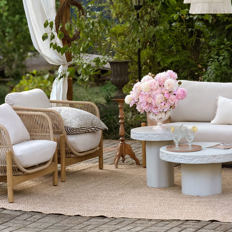 Tuinmeubelset met lichte kussens, rotan stoelen en betonnen tafels op jute vloerkleed buiten