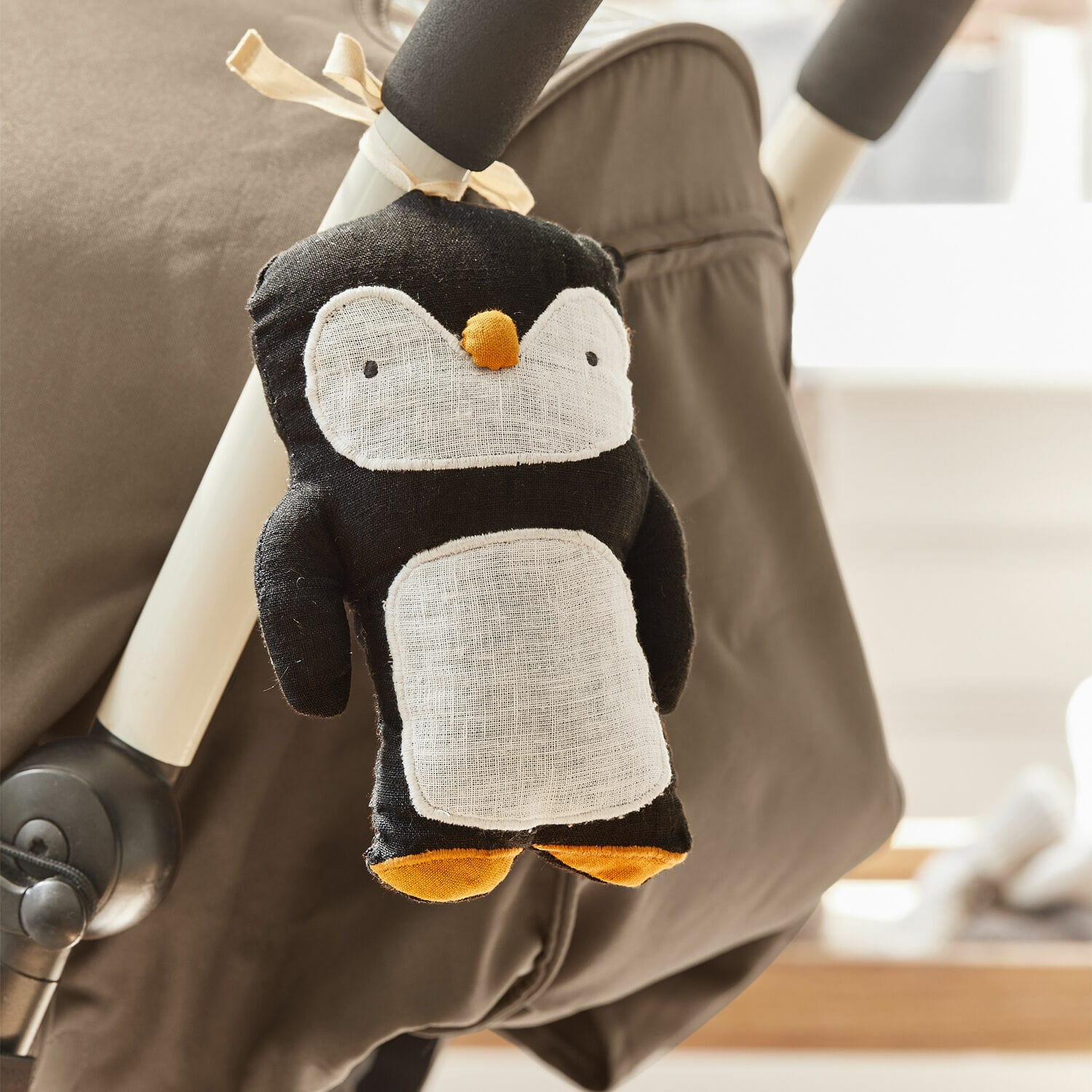 Pop voor aan de kinderwagen Jocienne Zwarte pluchen pinguïn met witte buik en oranje voeten bevestigd aan een kinderwagen