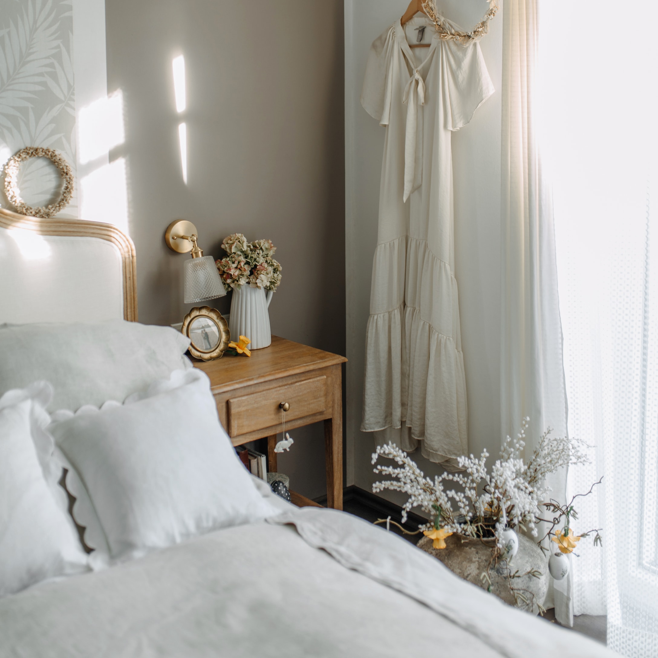 Gezellige slaapkamer met houten nachtkastje, wit beddengoed en crèmekleurige jurk aan de muur