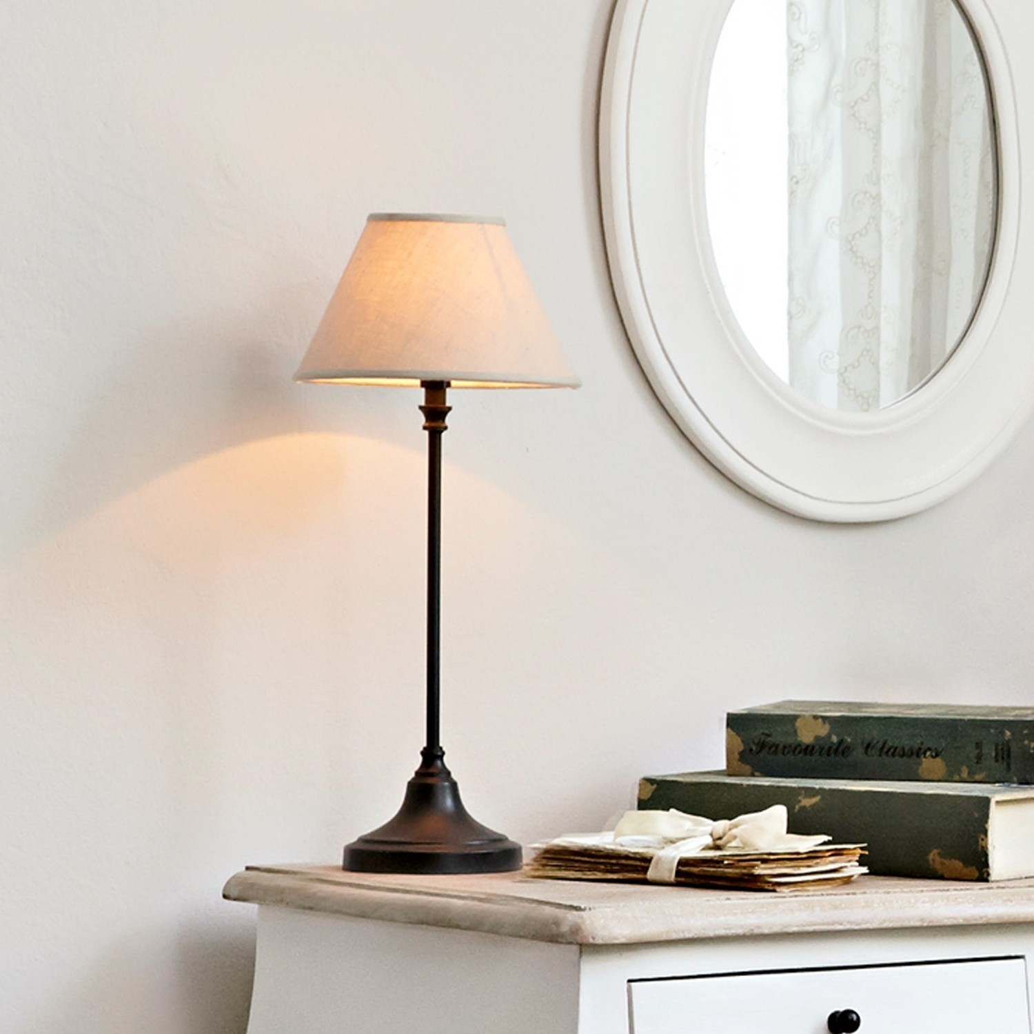 Tafellamp met zwarte metalen voet en beige kap op witte ladekast