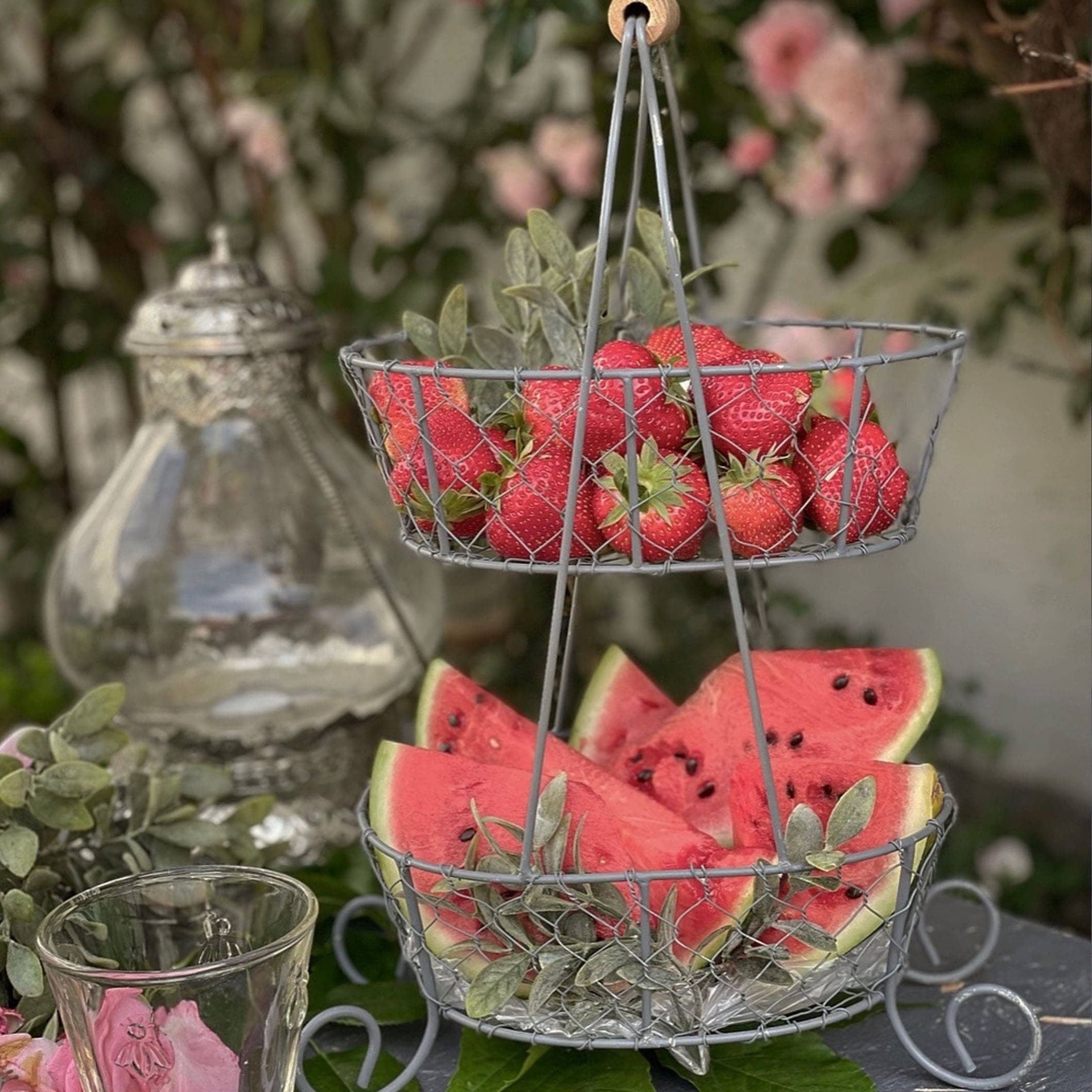 Tweeledige metalen mand met aardbeien en watermeloenpartjes voor zomerse tuintafel