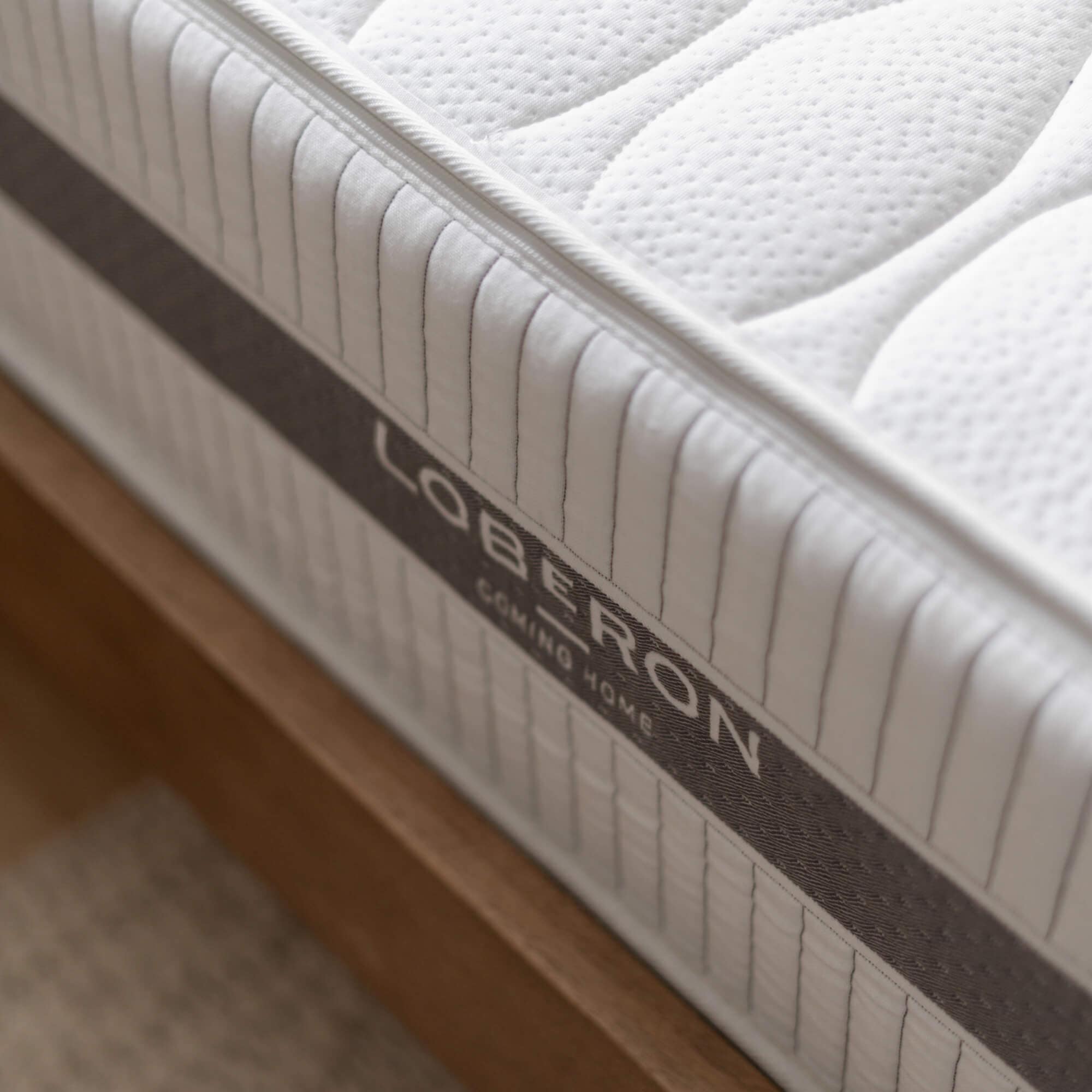 Witte doorgestikte matrasstof met grijze bies op houten bedframe