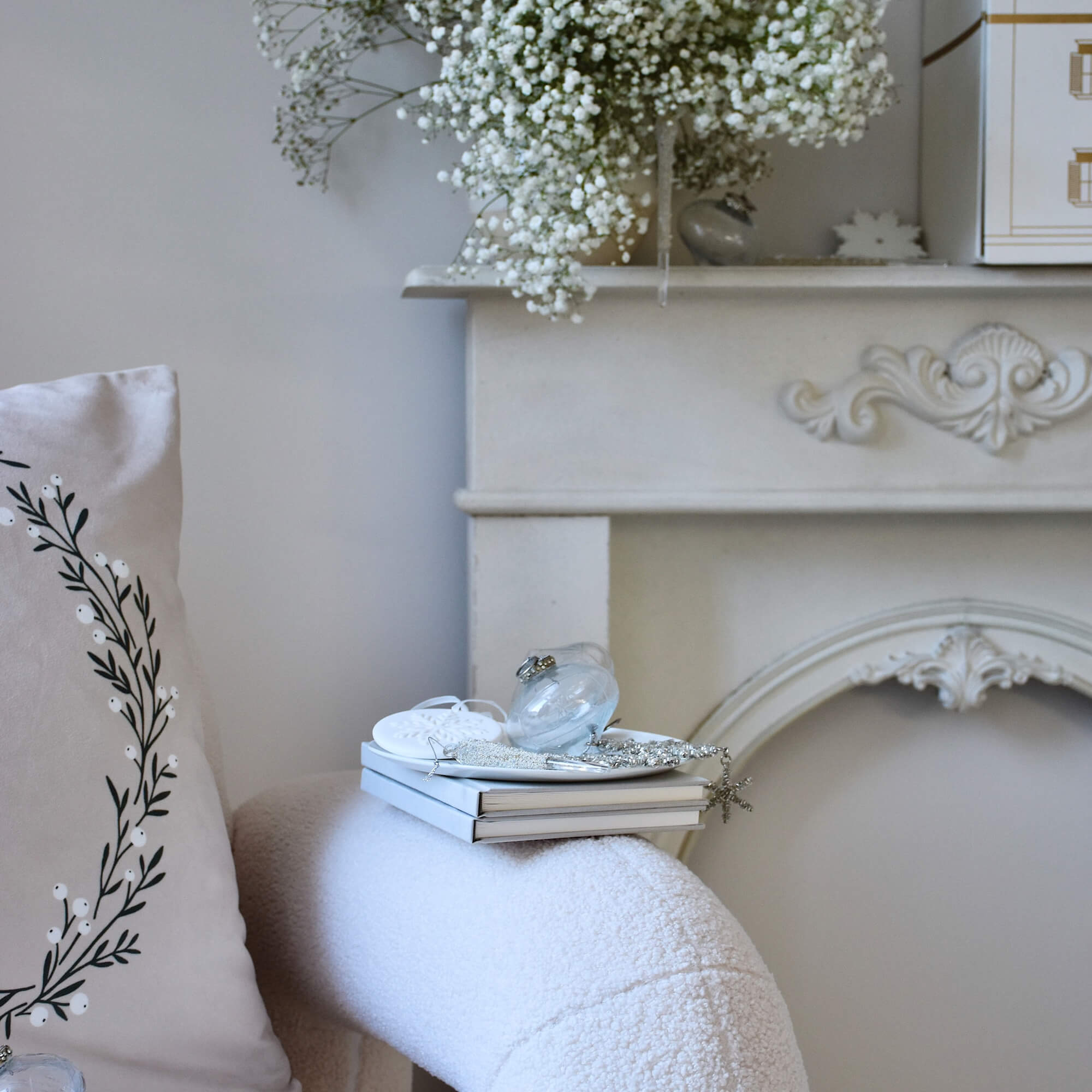 Witte decoratieve schoorsteenconsole met bloemen en boeken op zachte stoel in woonkamer