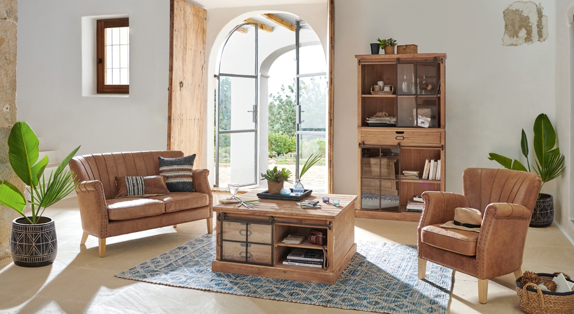 Woonkamer met lichte houten meubels, bruine leren bank en stoel op blauwe vloerkleed