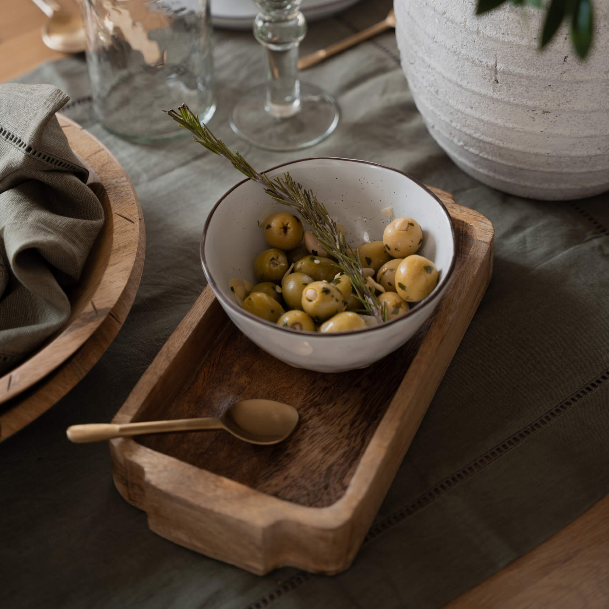 Witte keramische kom met groene olijven en rozemarijn takje op houten dienblad op tafel