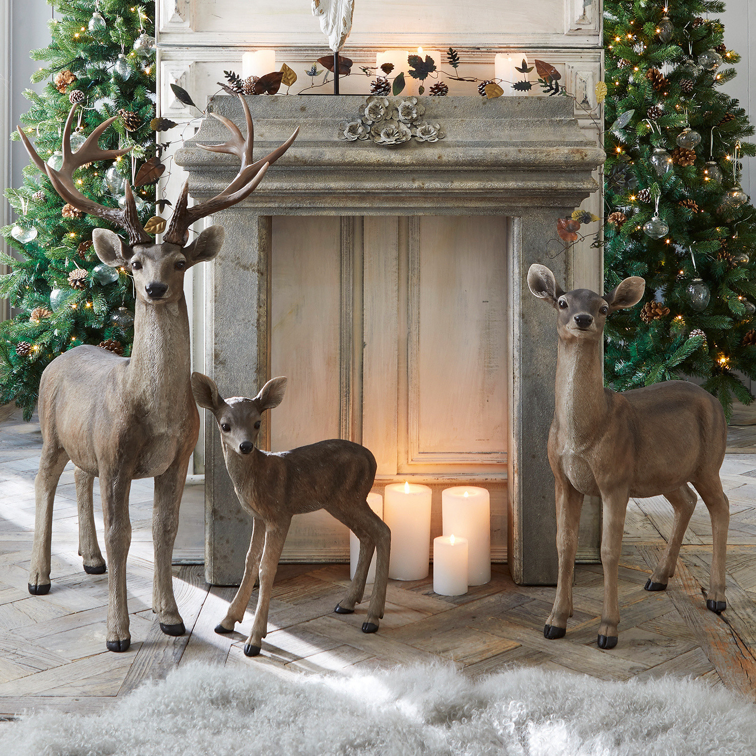 Hert met ree en reekalf Olsen Decoratieve figuren van drie bruine herten bij een open haard met brandende kaarsen en versierde kerstbomen