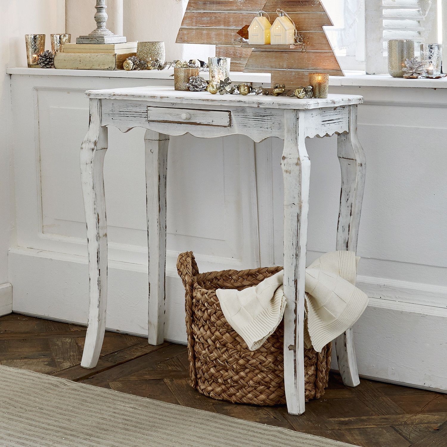 Witte houten vintage tafel met lade, kerstdecoraties en gevlochten mand op de vloer