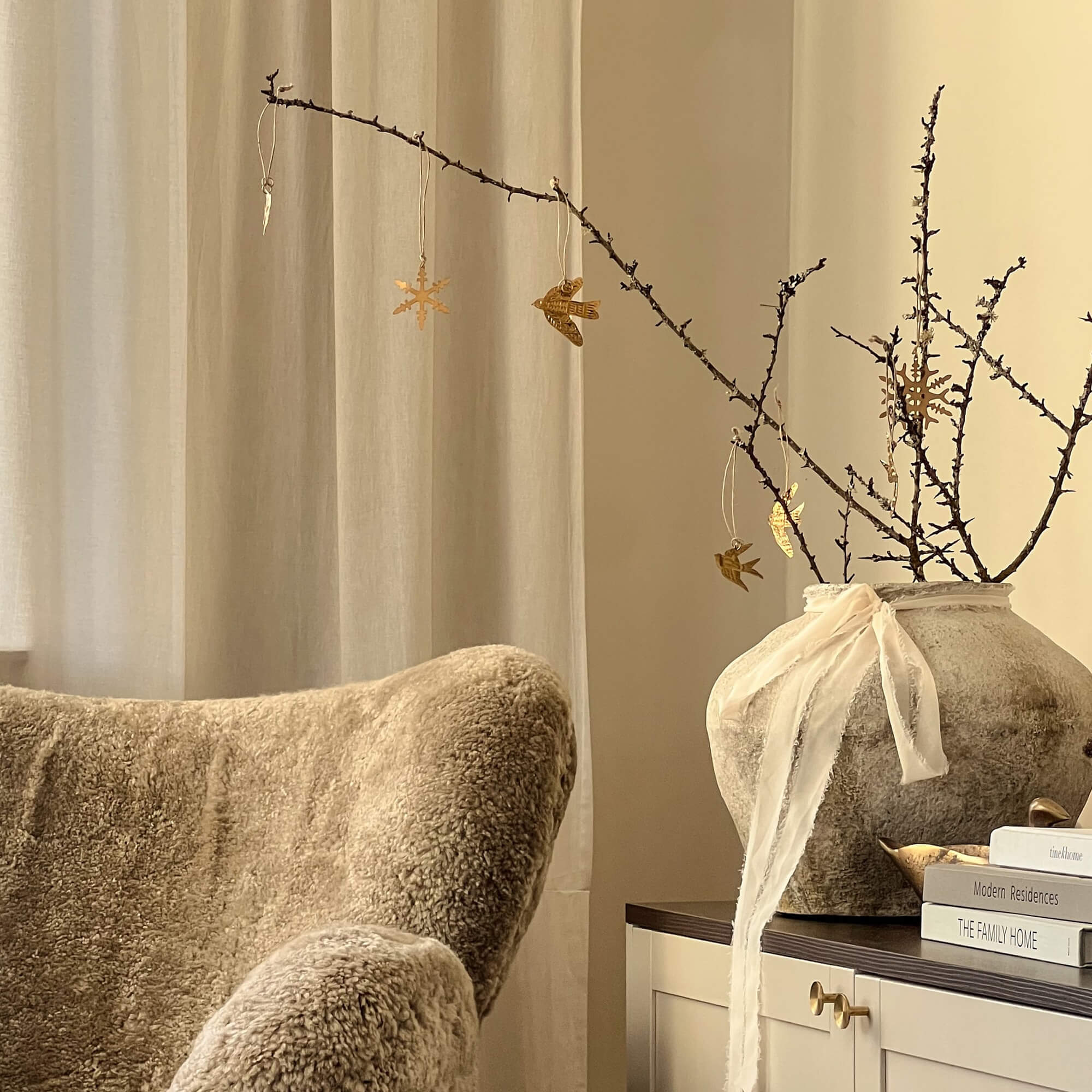 Gezellige hoek met beige faux fur stoel en decoratieve vaas met takken en gouden versieringen