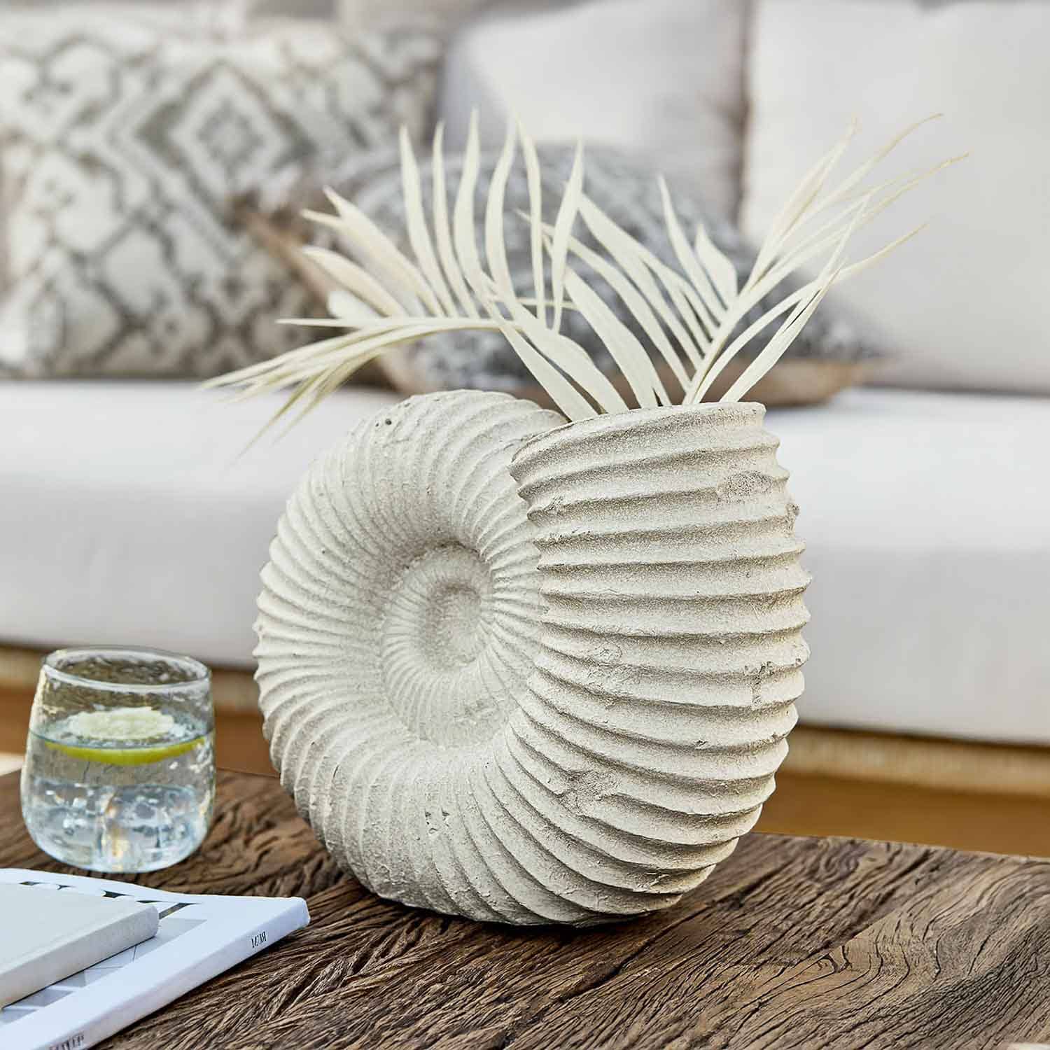 Decoratieve vaas van lichtsteen in schelpvorm met gedroogde bladeren op houten tafel