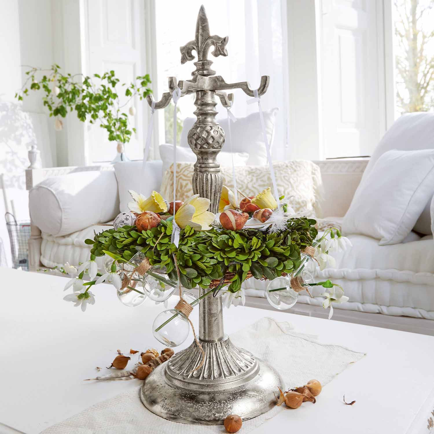 Metalen tafeldecoratie met groene krans en glazen bollen op witte tafel in lichte woonkamer