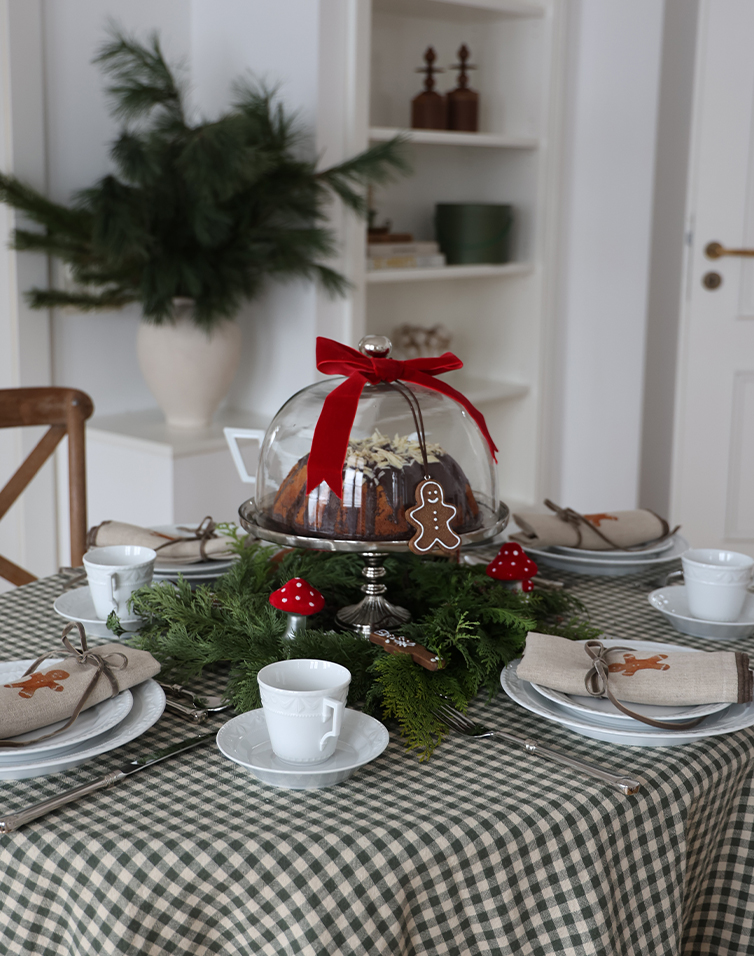 Feestelijk gedekte tafel met cake onder glazen stolp, groene takken en rode paddenstoelen decoratie