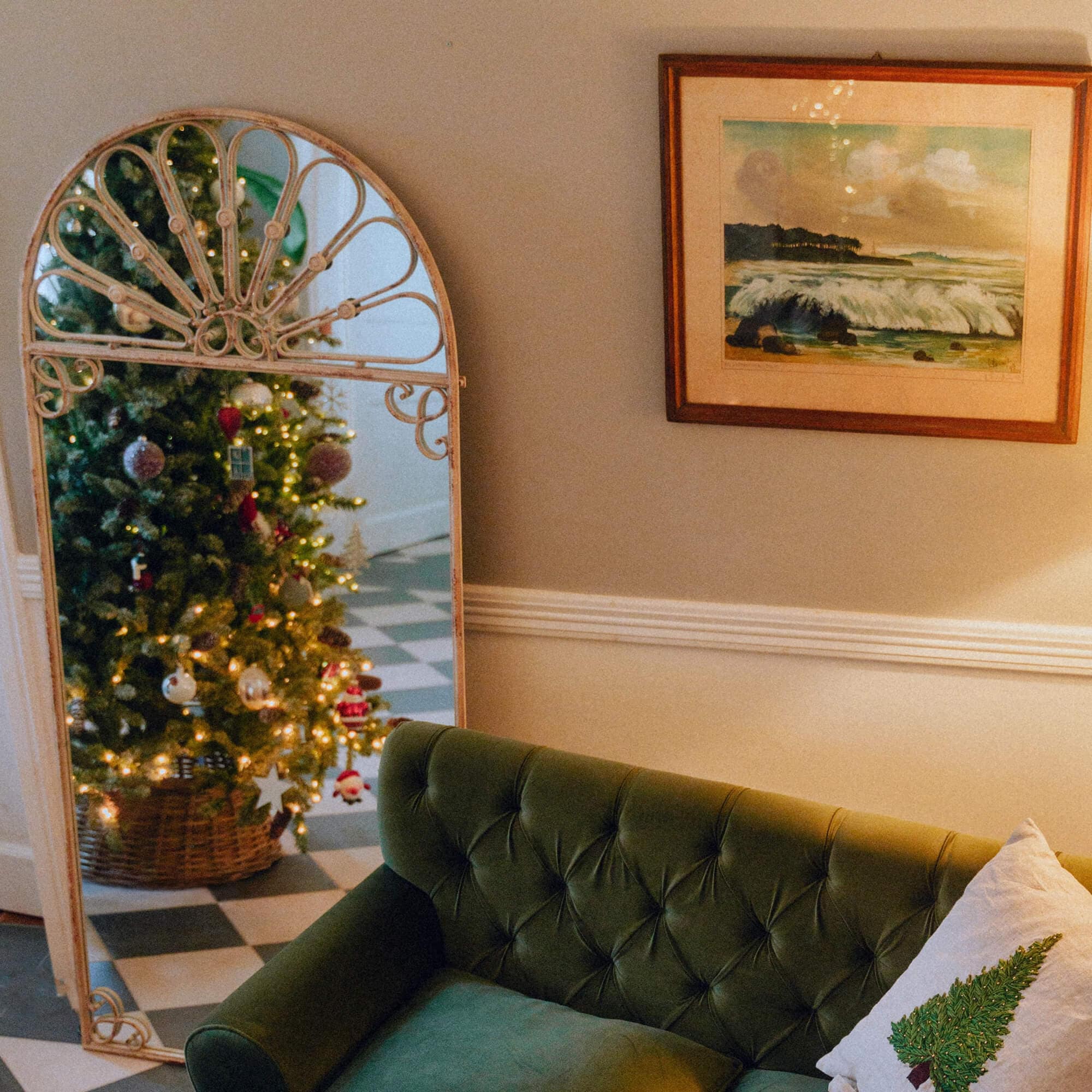 Decoratieve spiegel met metalen lijst die een kerstboom weerspiegelt in een gezellige woonkamer met groene bank