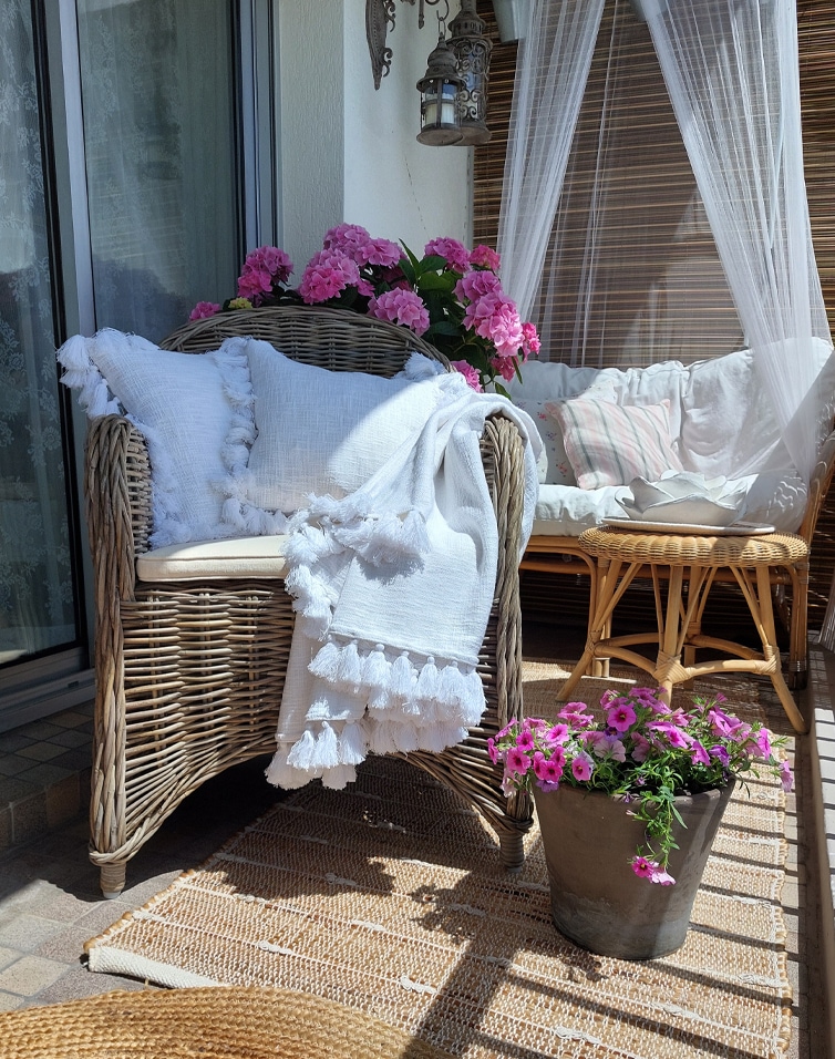 Gezellig balkon met rotan stoel, witte deken en roze bloemen, stijlvolle terrasdecoratie