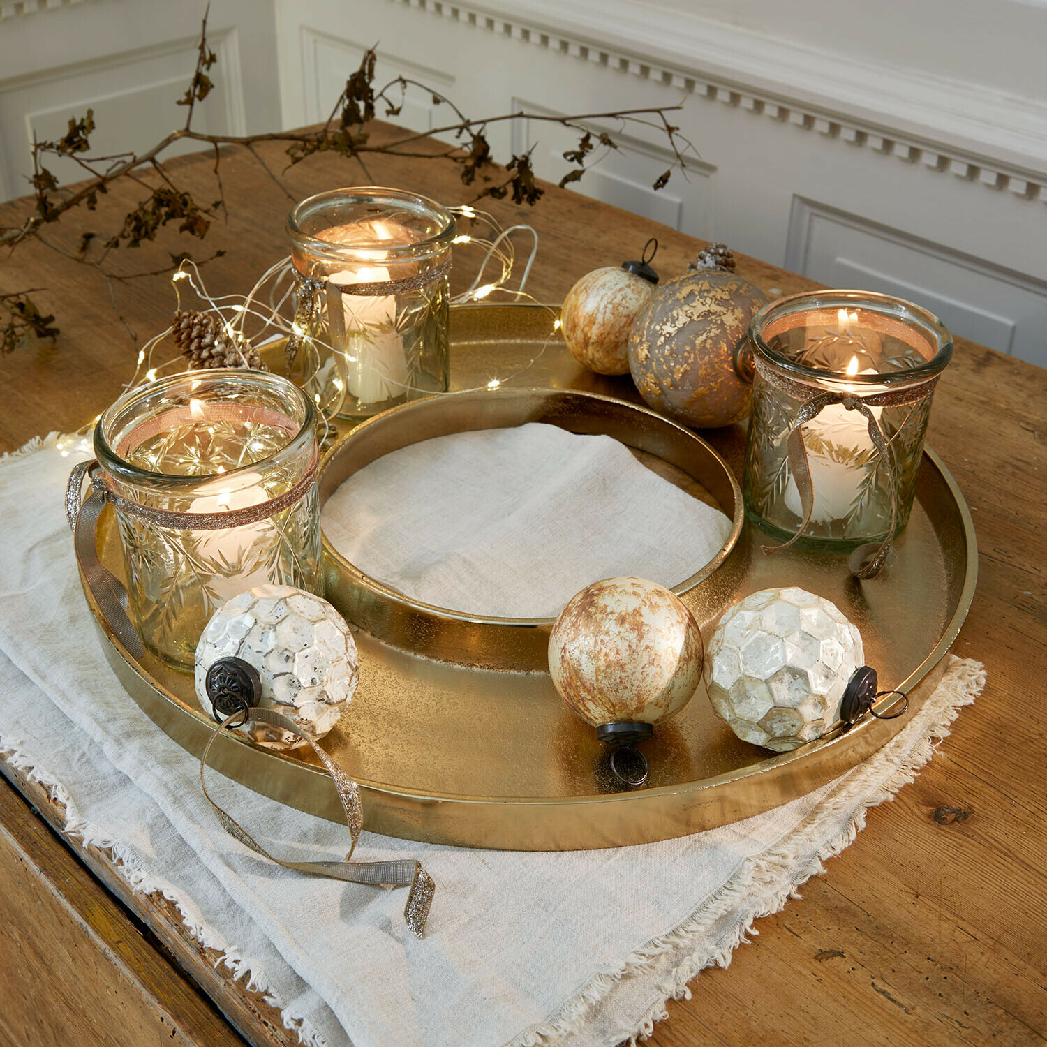 Kaarsenplateau Velarosas Gouden metalen dienblad met drie glazen windlichten en decoratieve ballen op houten tafel