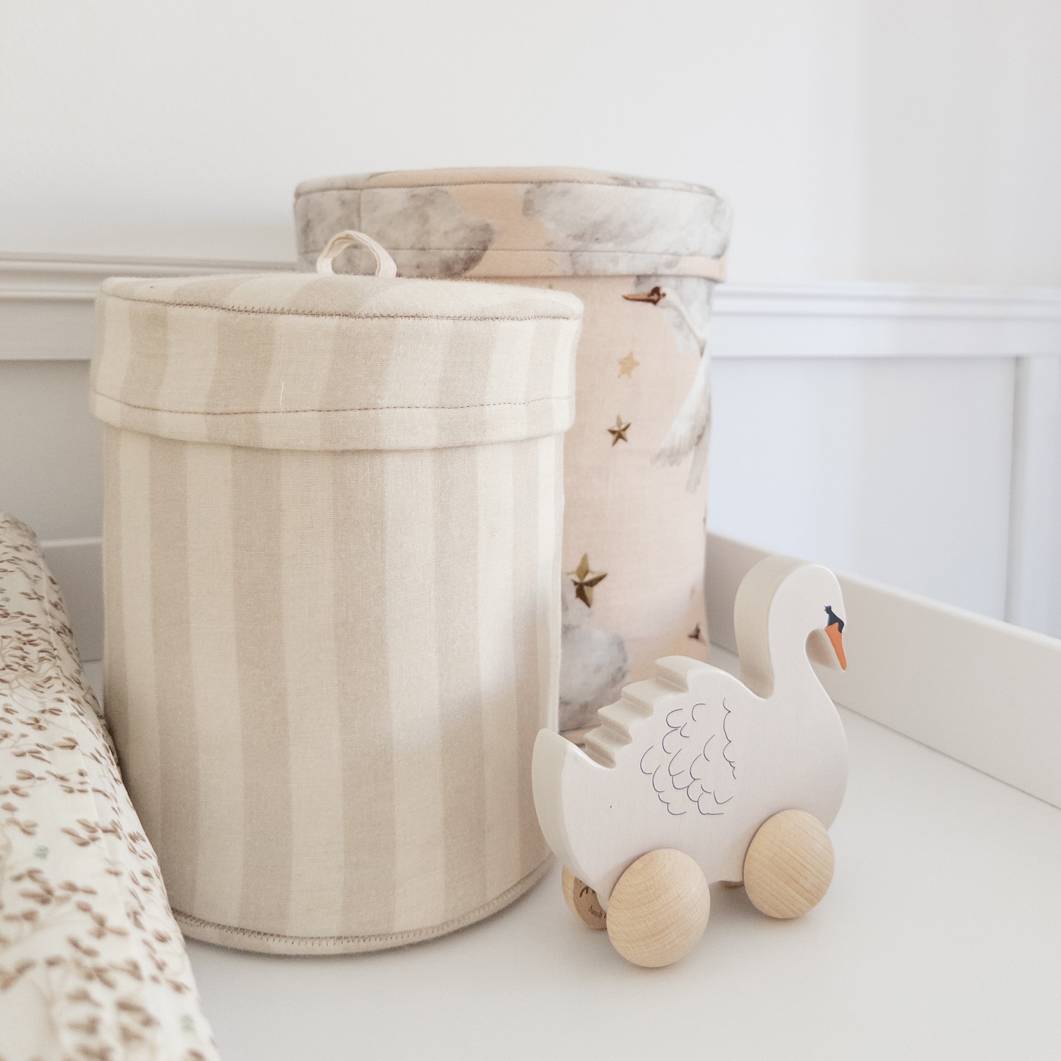 Houten zwaan speelgoed op wielen naast beige stoffen opbergdozen in kinderkamer