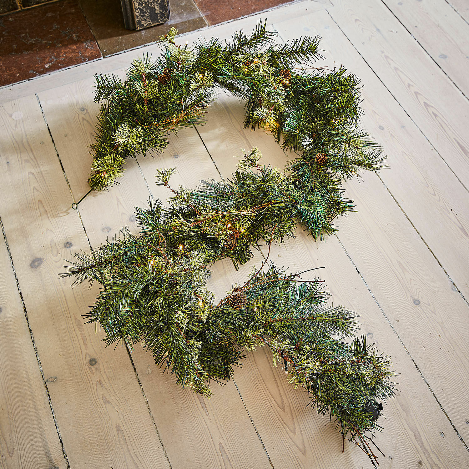 Ledguirlande Enquilo Kerstkrans met groene naalden, kleine dennenappels en warme LED-verlichting op lichte houten vloer