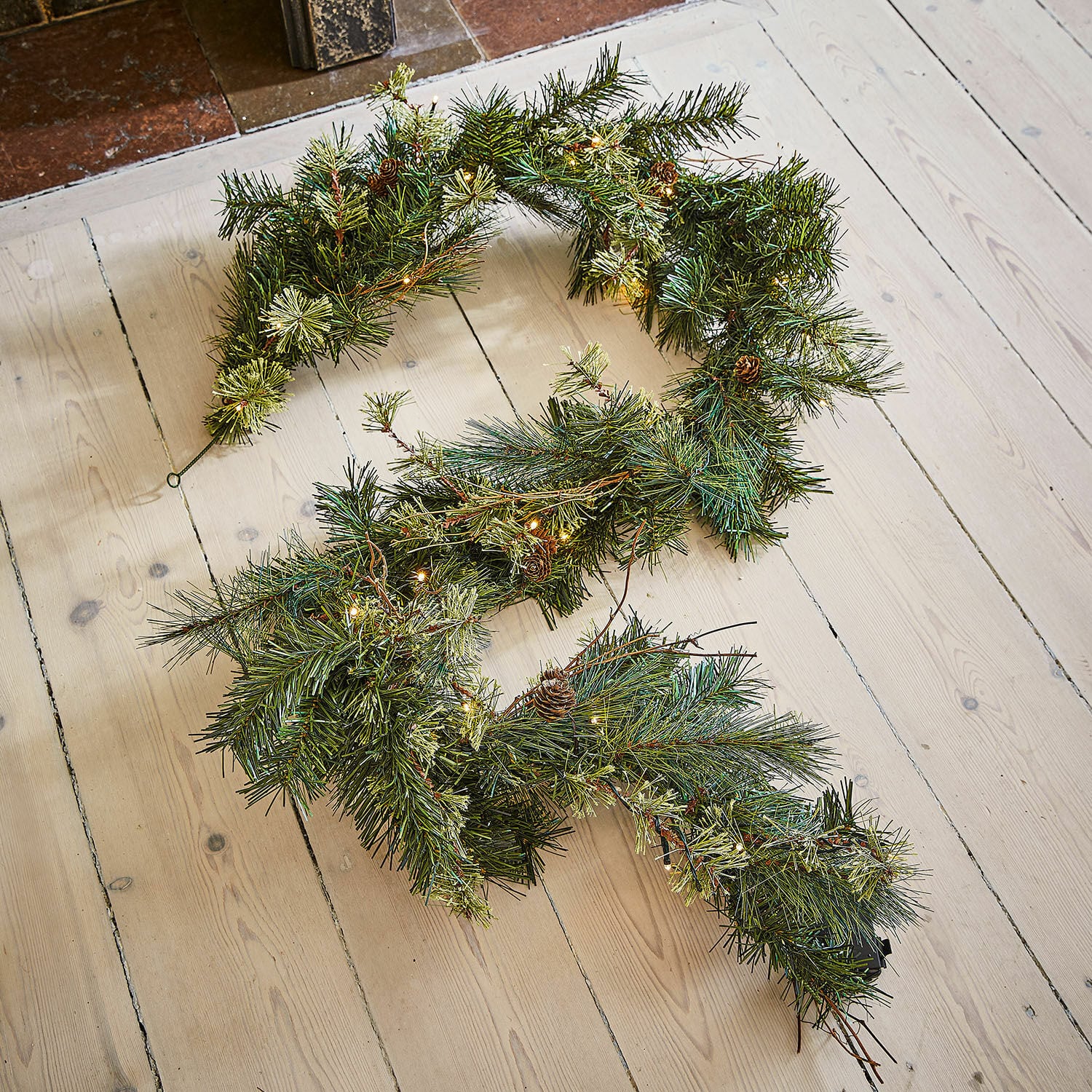 Ledguirlande Enquilo Kerstkrans met groene naalden, kleine dennenappels en warme LED-verlichting op lichte houten vloer