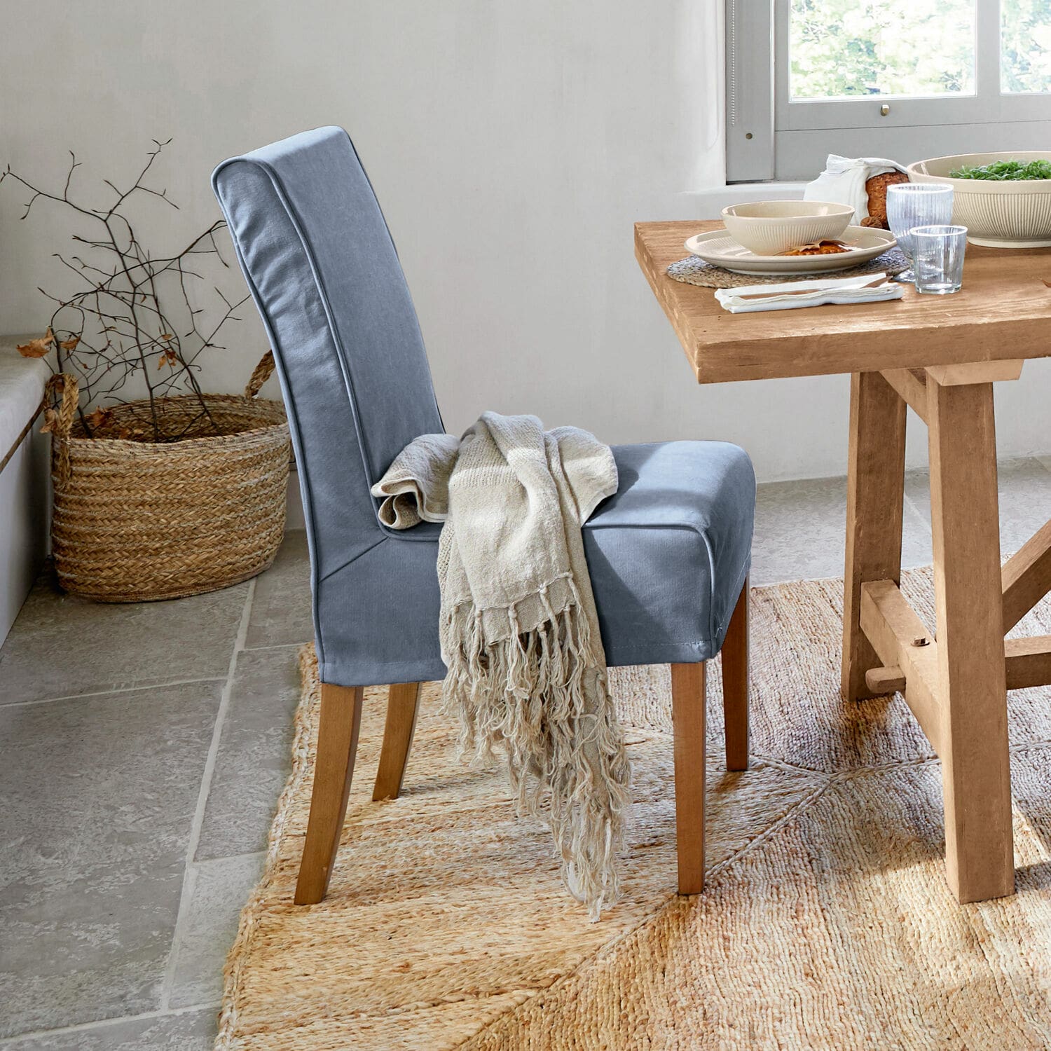 Blauw gestoffeerde stoel met houten poten en beige deken bij lichte houten tafel