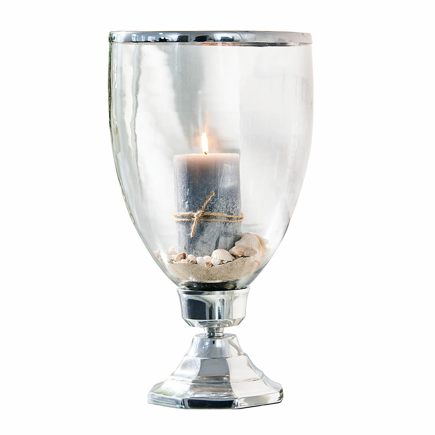 Glazen windlicht met metalen voet en grijze kaars op zand met schelpen, woondecoratie