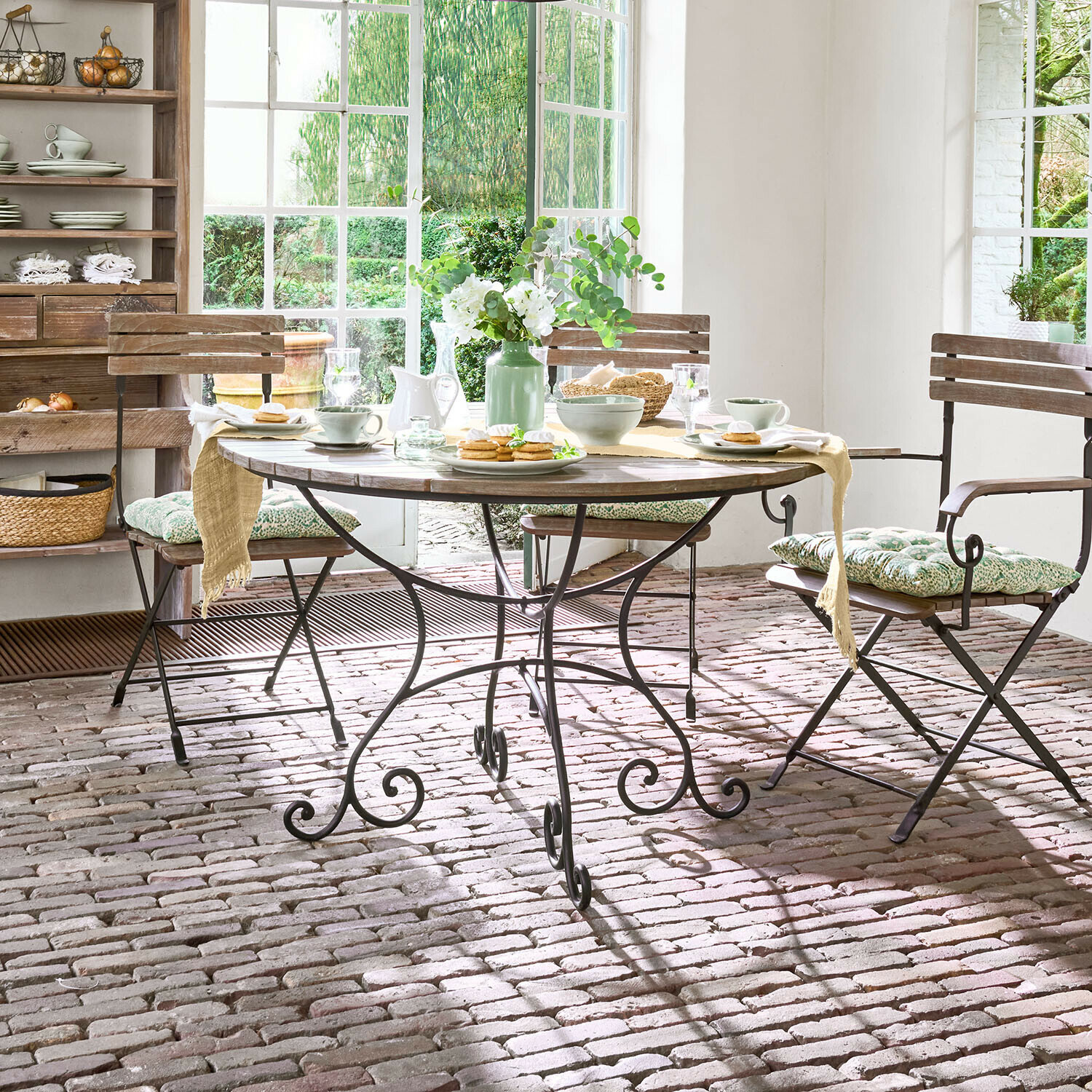 Ronde houten tafel met metalen onderstel in rustieke eetkamer met stoelen en bloemendecoratie